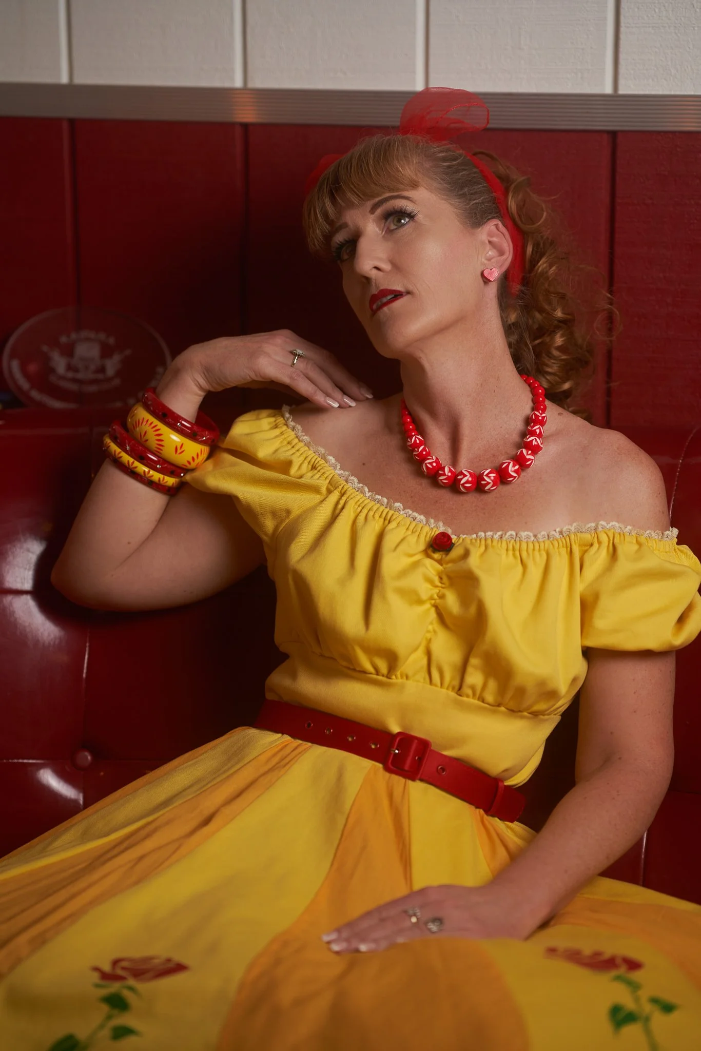 Sandy poses in a red booth in her yellow dress