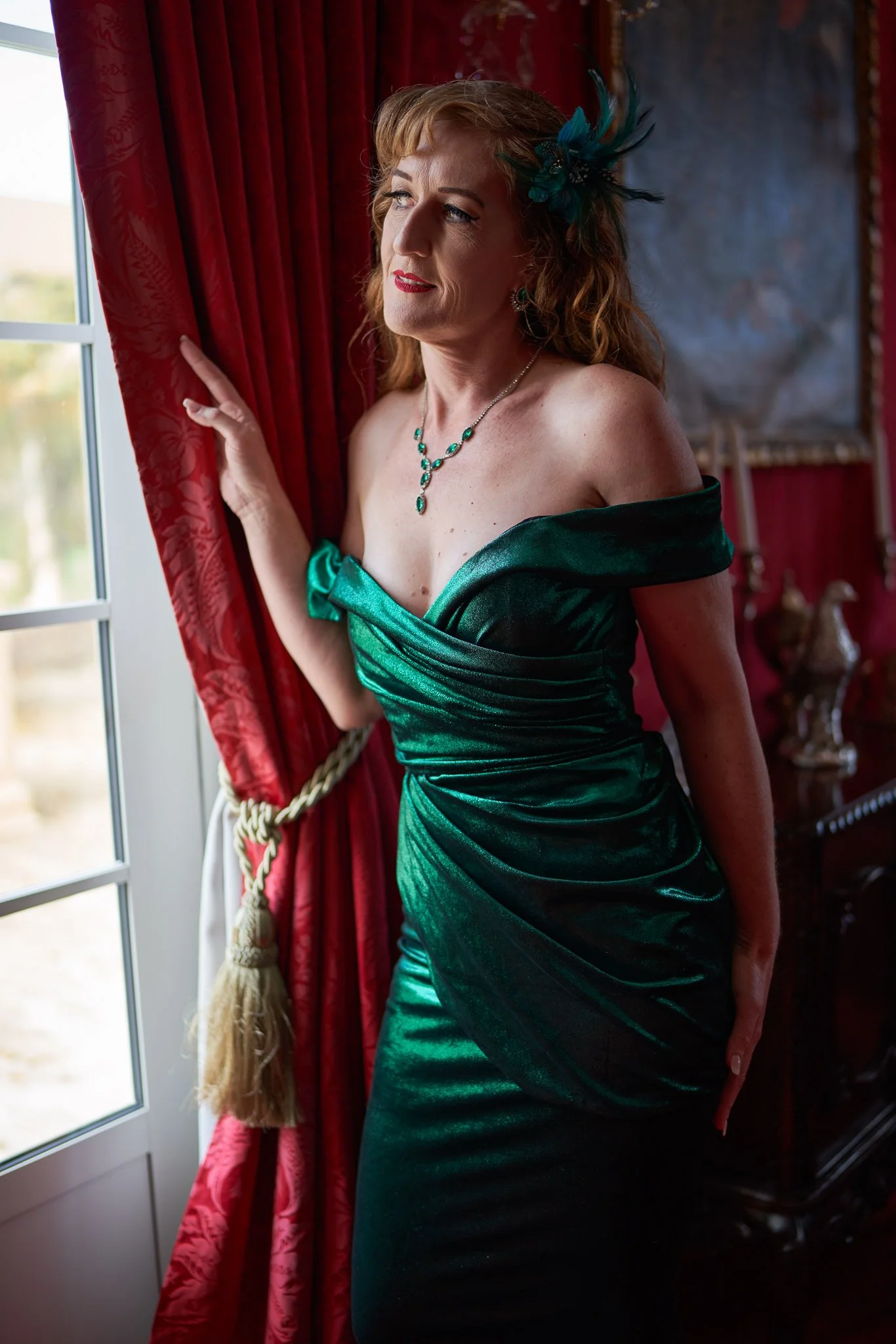 Sandy in green satin holding the curtain by a window