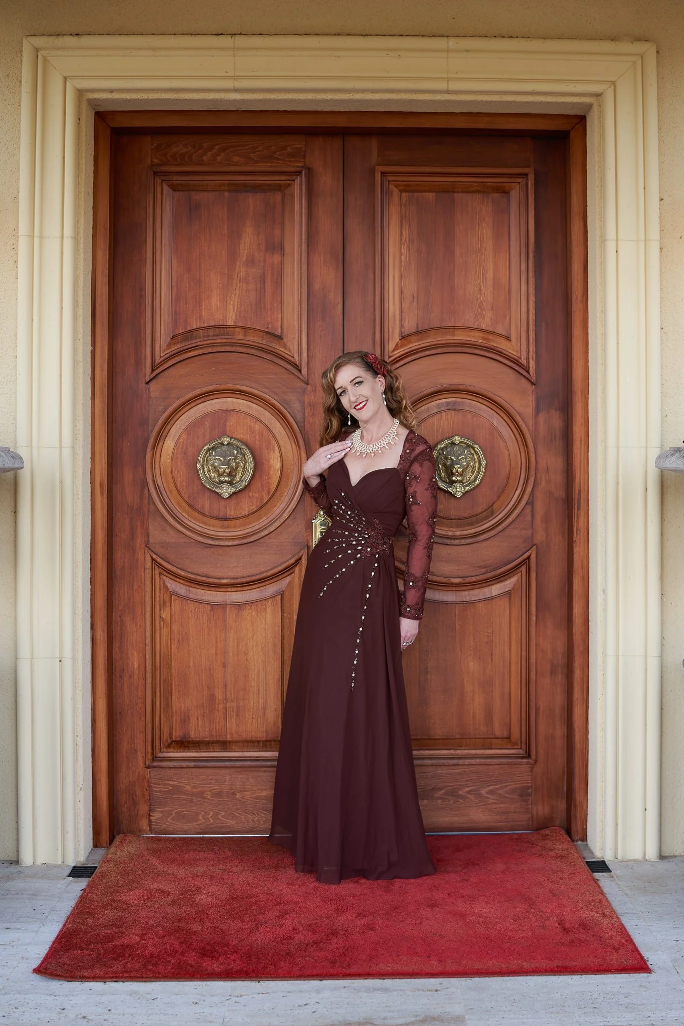 Sandy in a burgundy gown before grand wooden doors