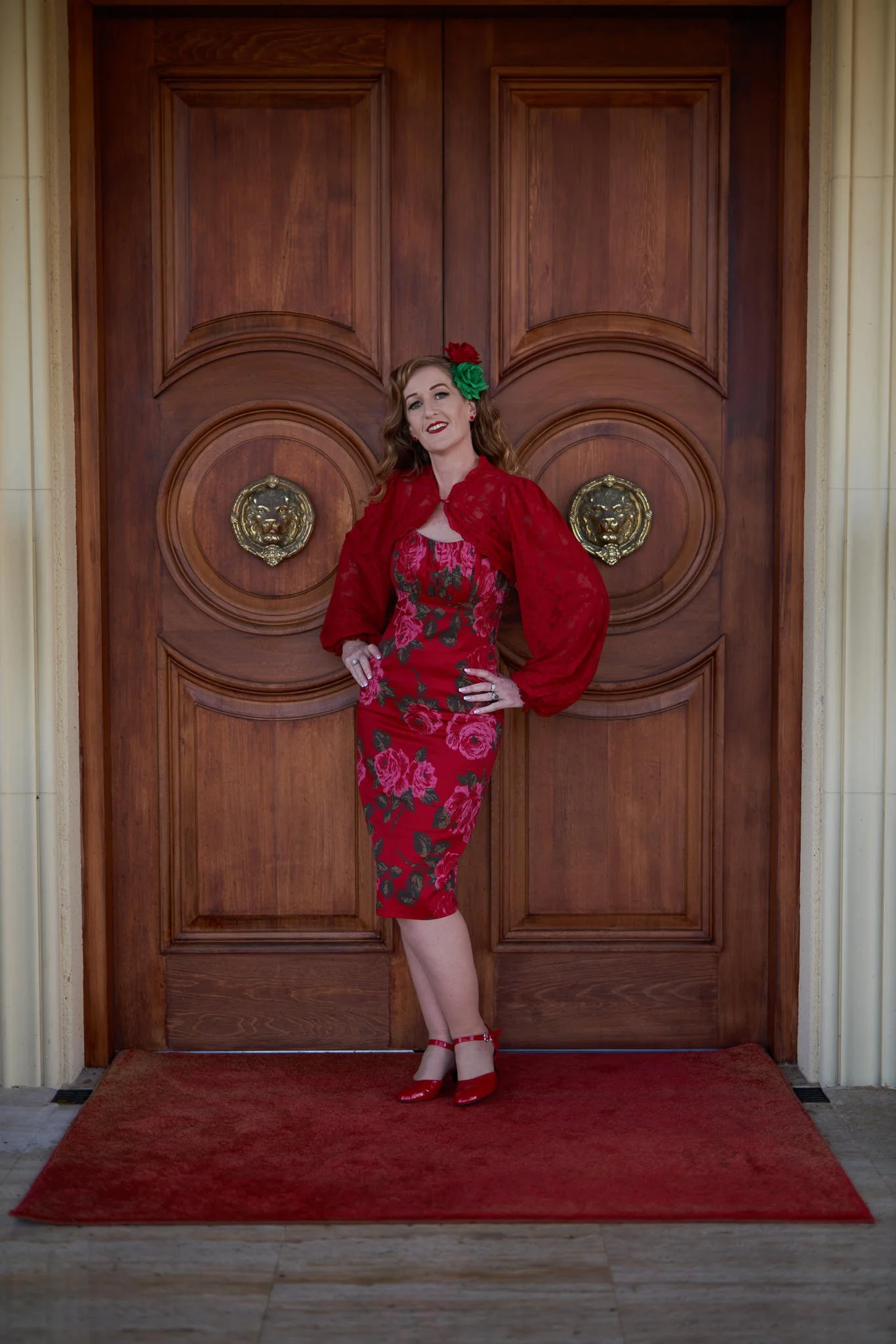 Sandy in a red rose-print dress before wooden doors