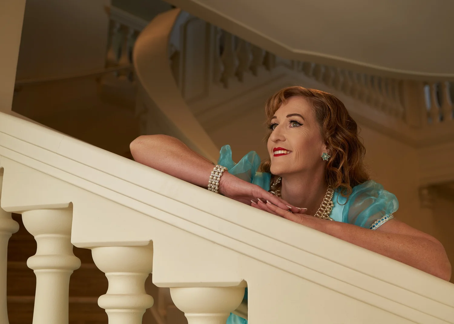 Sandy leans on a curved staircase banister