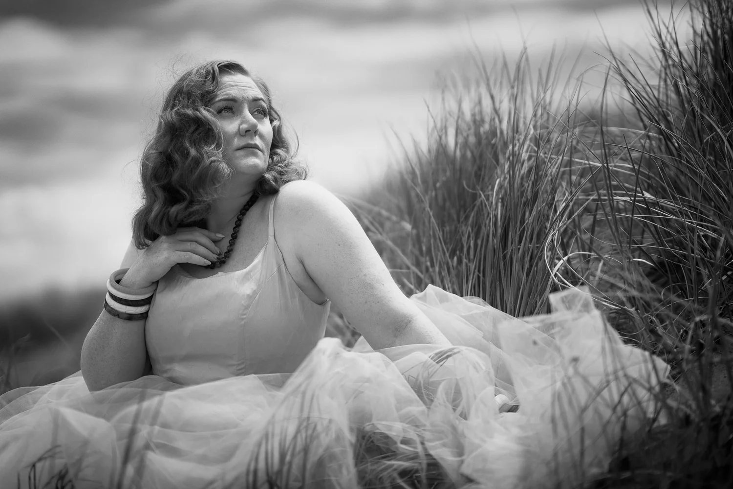 Black and white photo of a model reclining in the dunes at Muriwai Beach