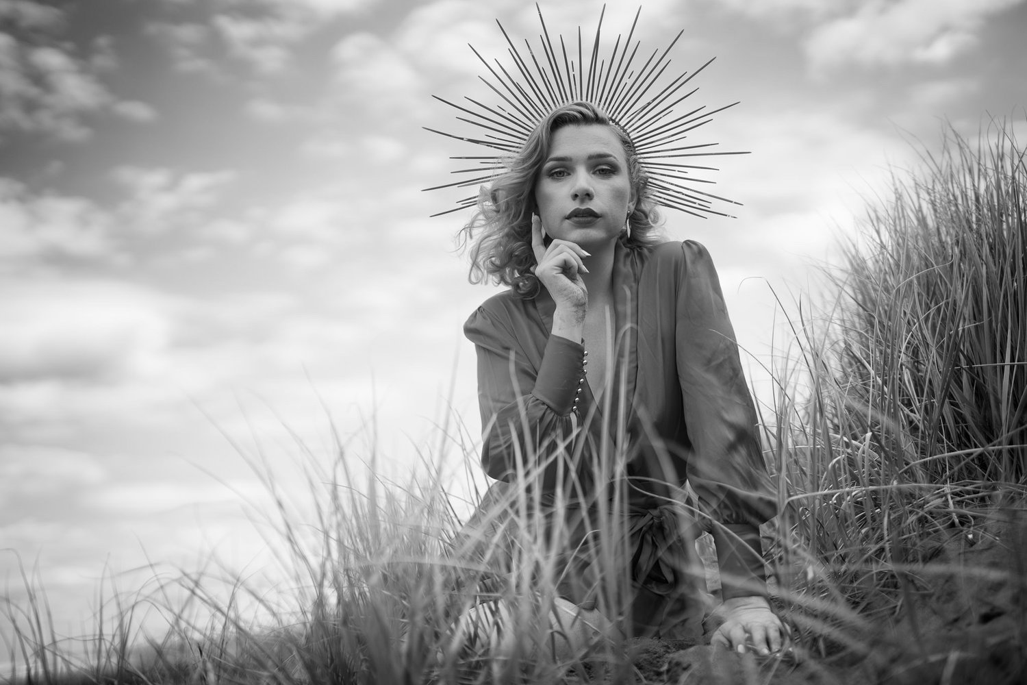 Black and white photo of a model in a spiked crown among the grasses
