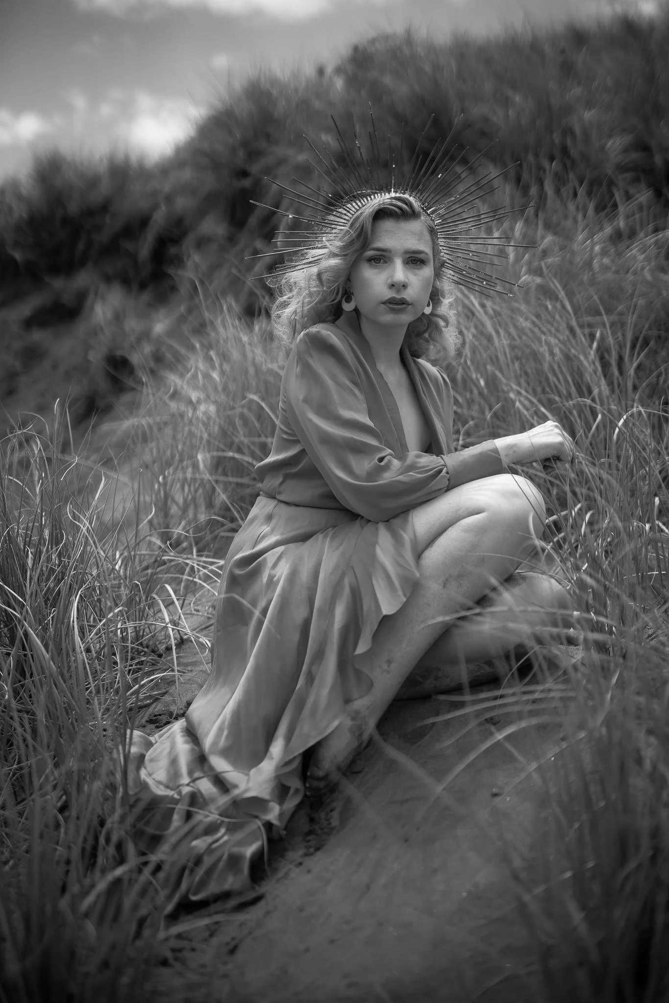 Black and white photo of a model sitting in the dune grasses
