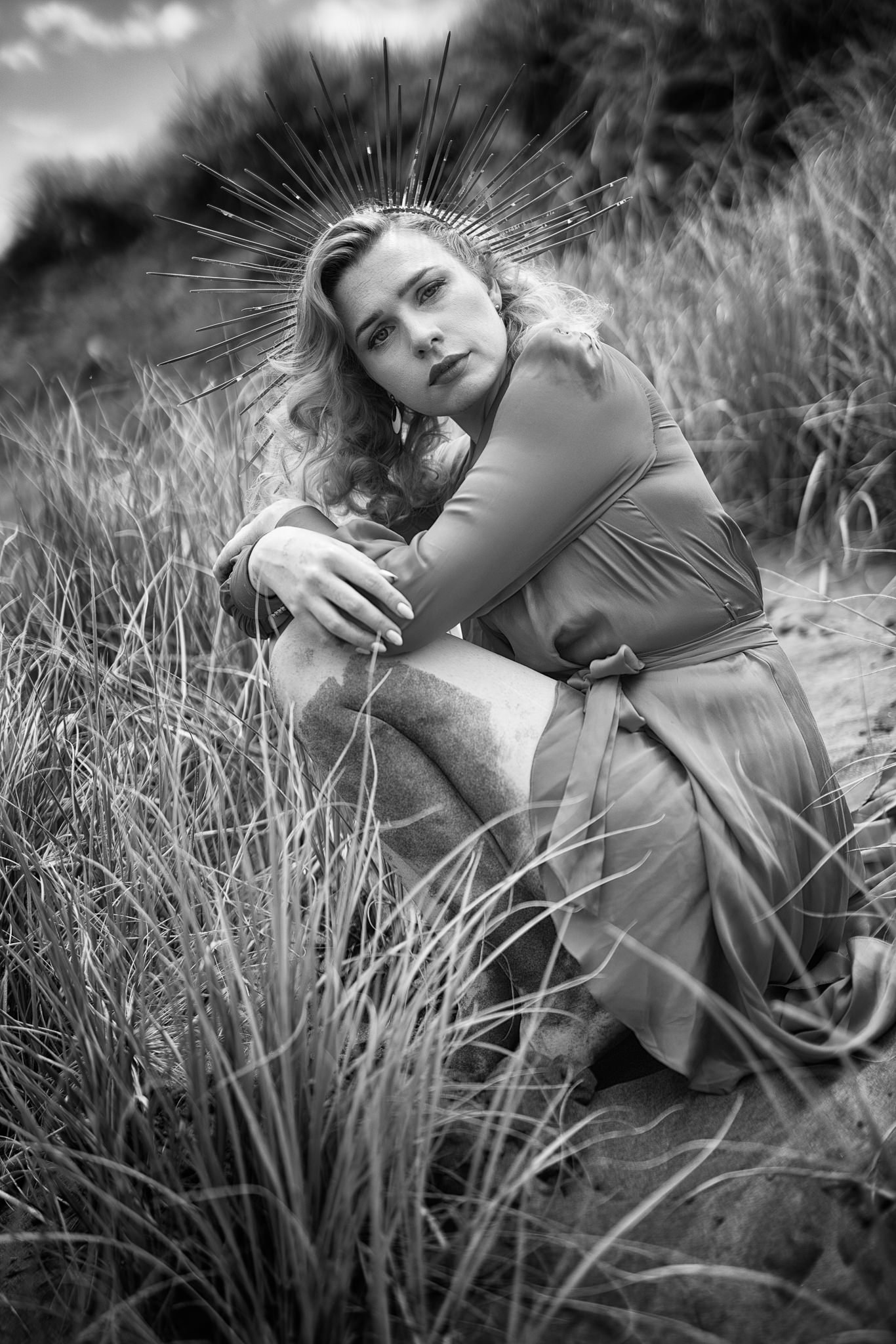 Black and white photo of a model in a crown hugging her knees