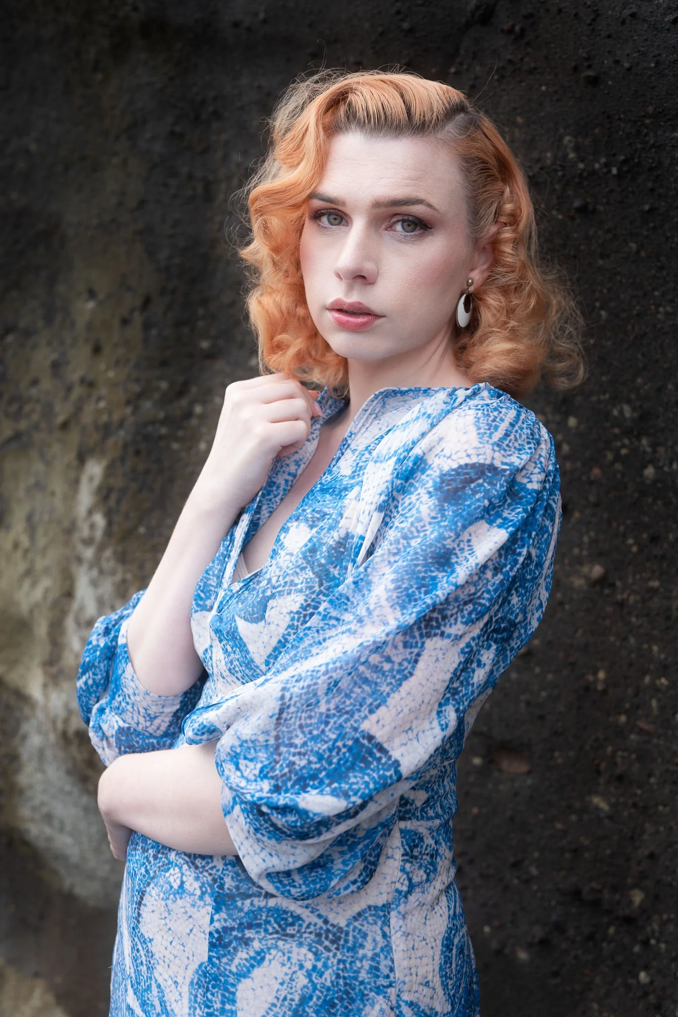 A model in a blue patterned dress against a dark rock wall