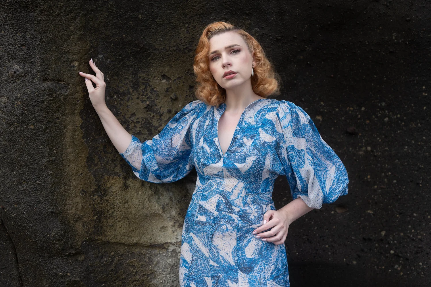 A model in a blue dress posing against a black rock face