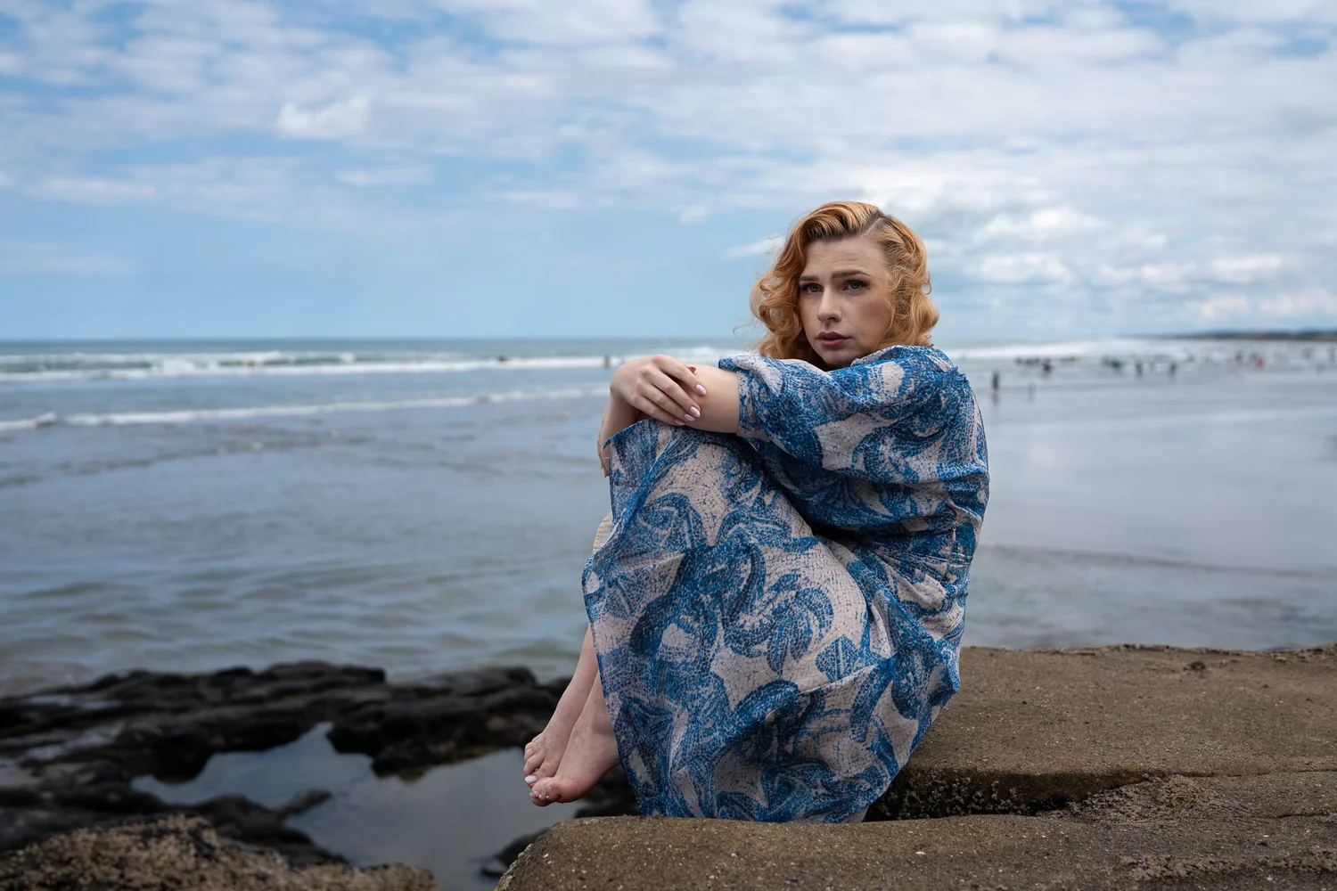 A model in a blue dress sits on the rocks at Muriwai