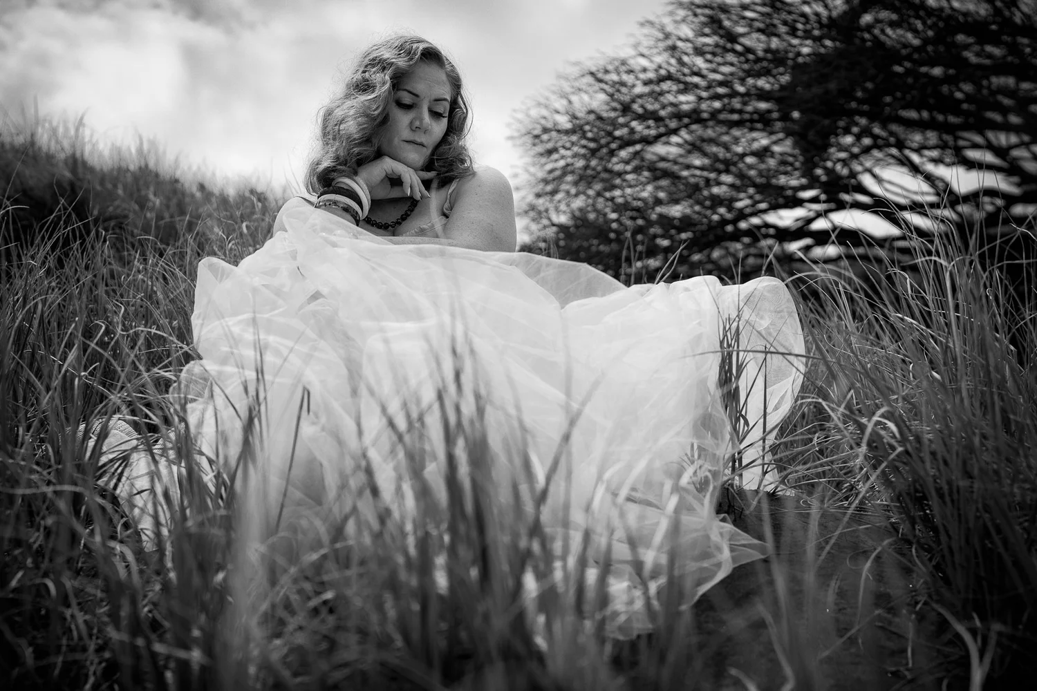 Black and white photo of a model in a full white dress in the dunes
