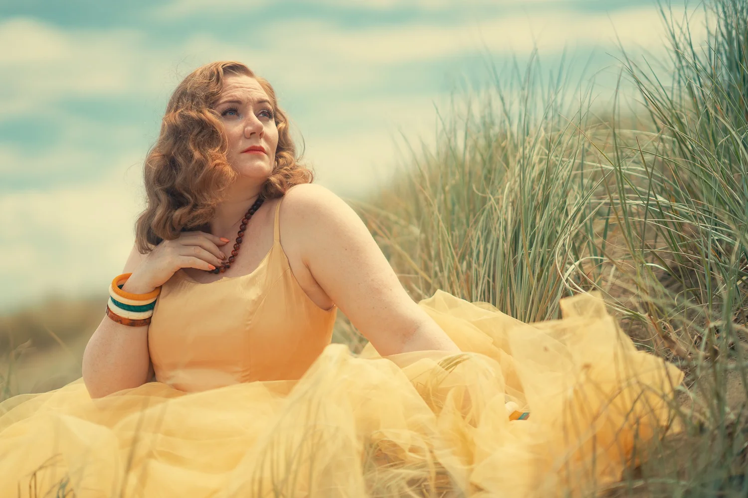 A model in a peach tulle dress reclines in the dune grasses
