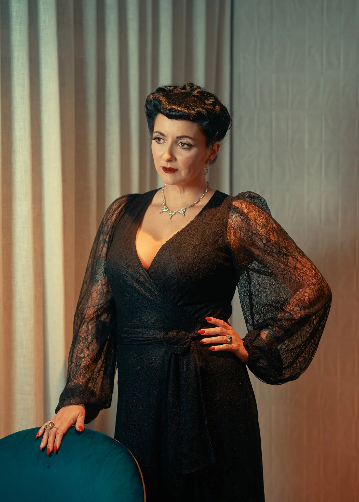 Viv in a black lace gown with a hand on her hip