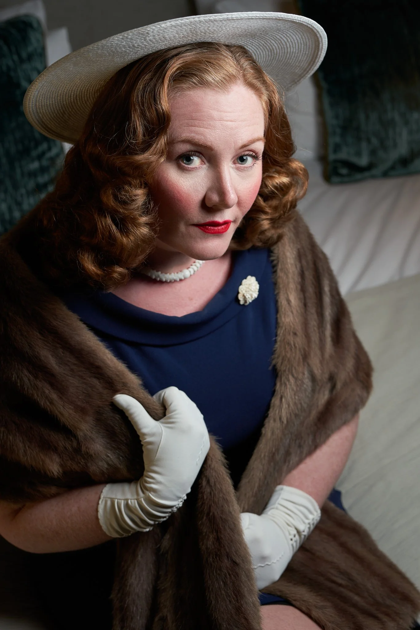 Laura in a white hat and fur stole looking at the camera