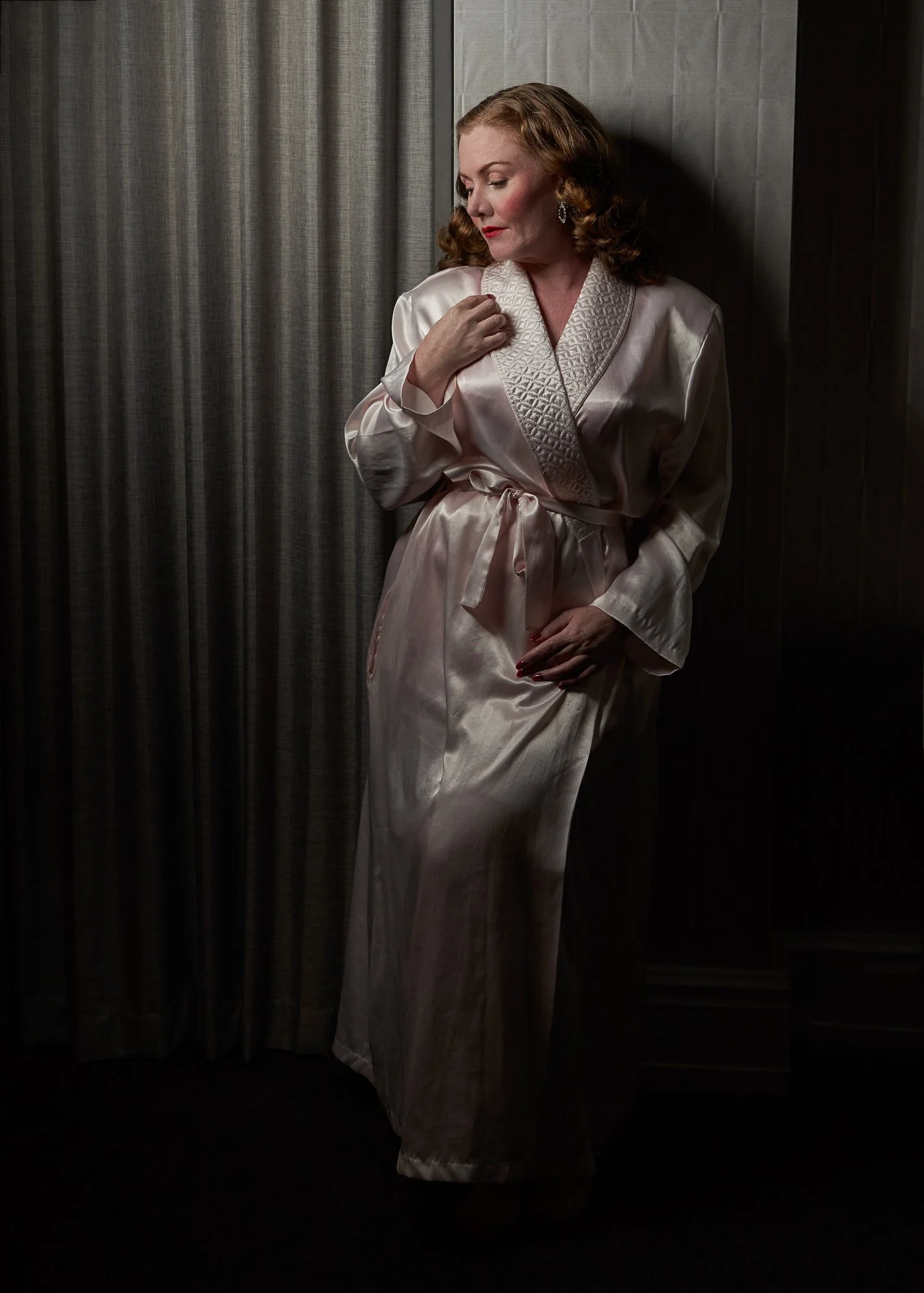 Laura in a pink satin robe beside a curtain