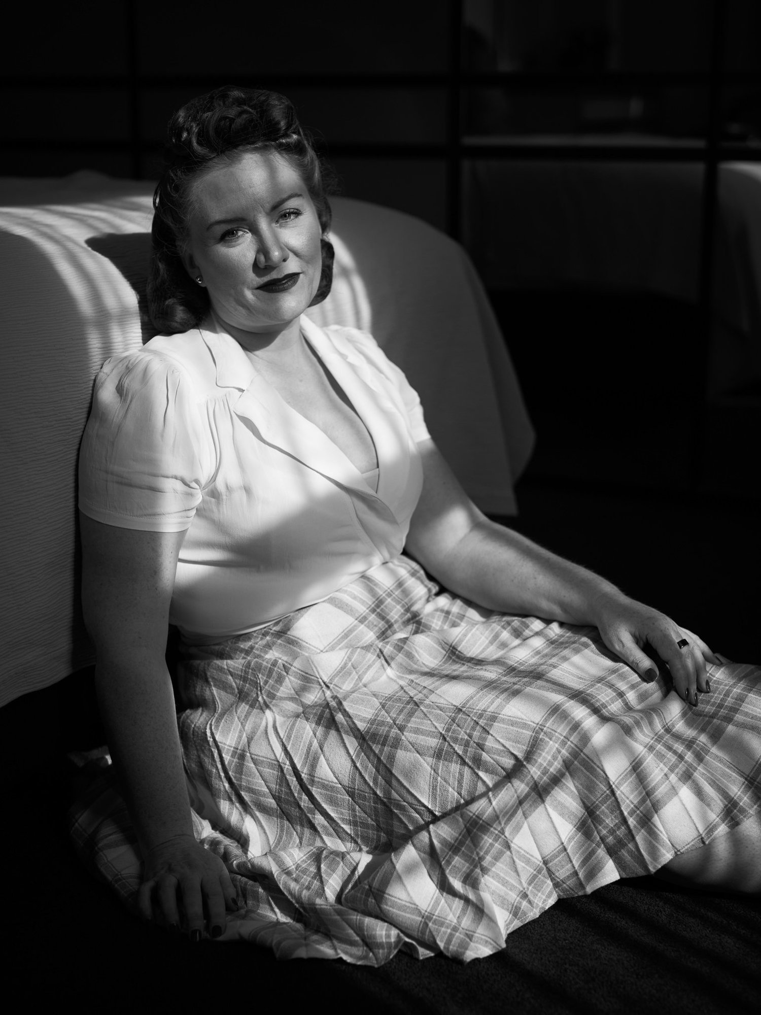 Black and white photo of Laura sitting on the floor in a 1940s outfit