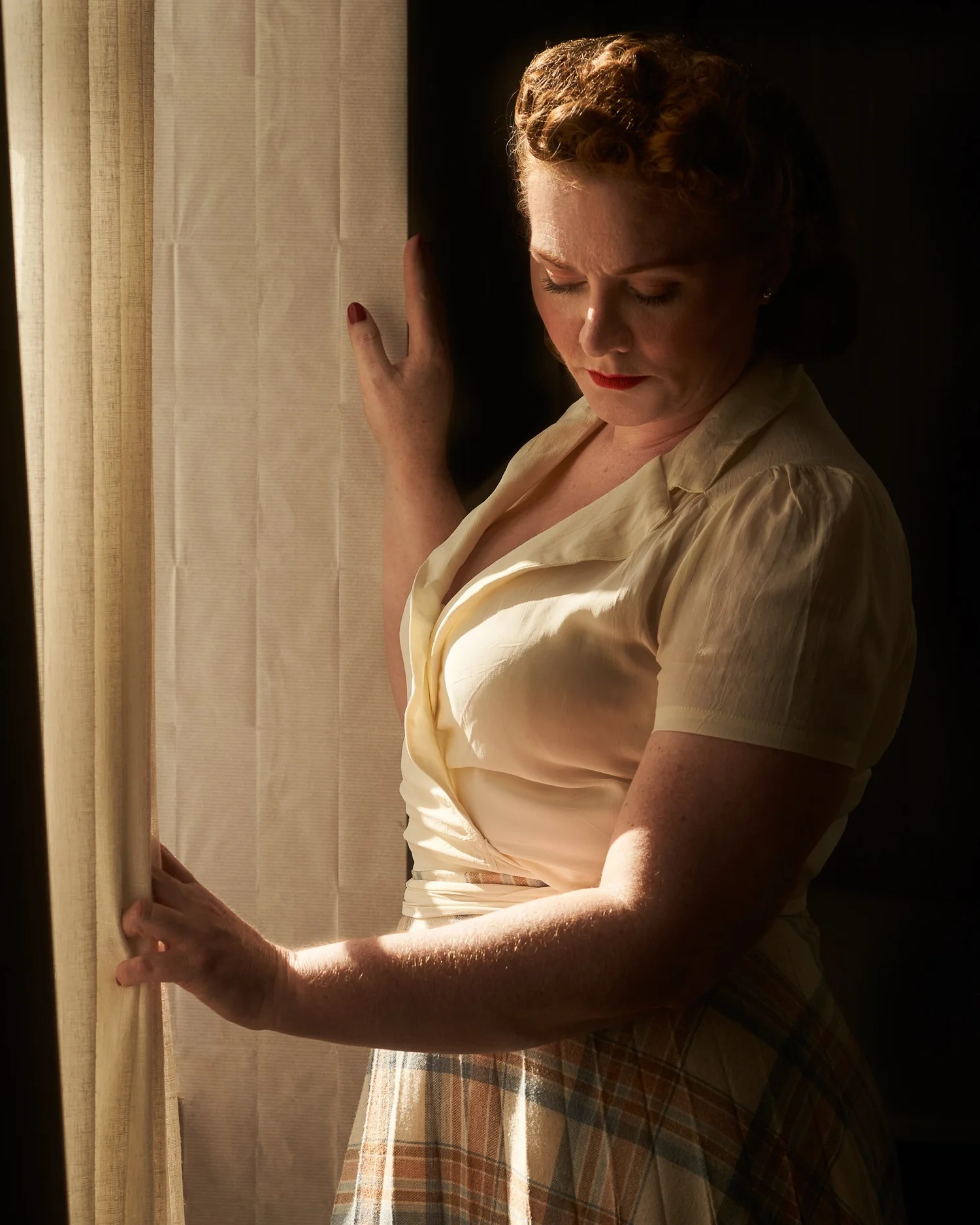 Laura in a vintage outfit holding back a curtain