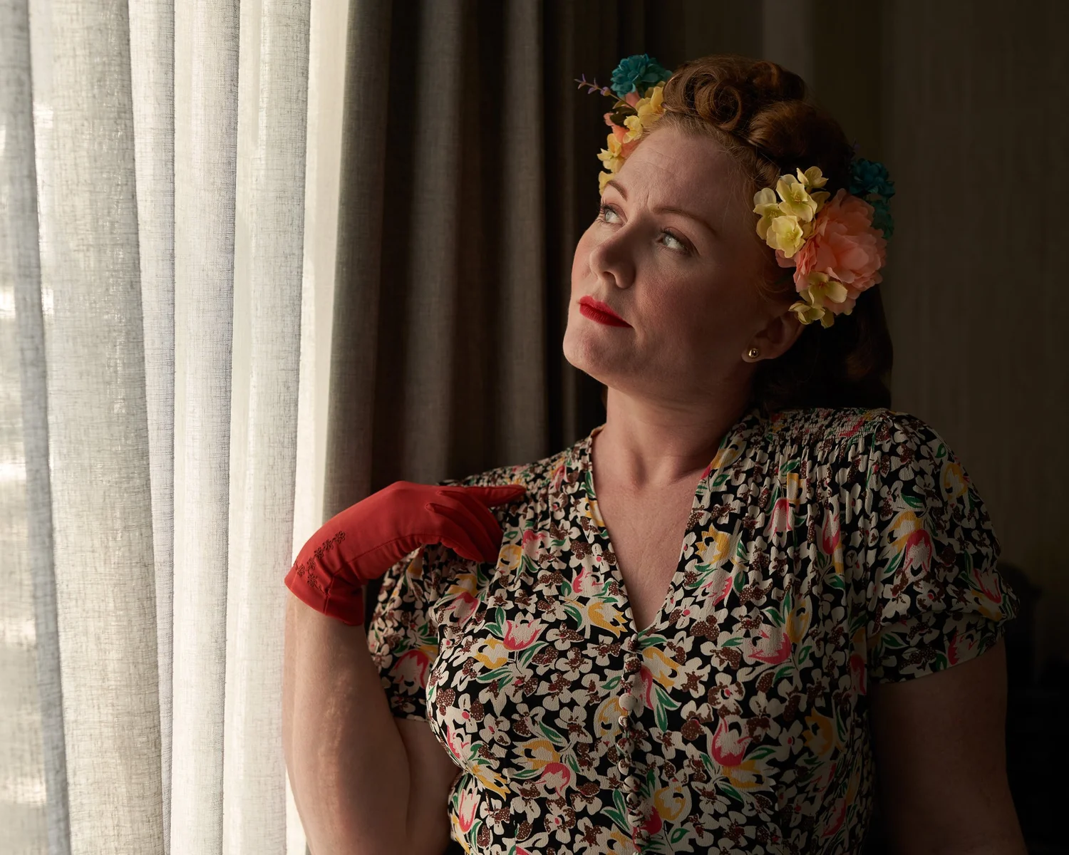 Laura with flowers in her hair and red gloves by a window