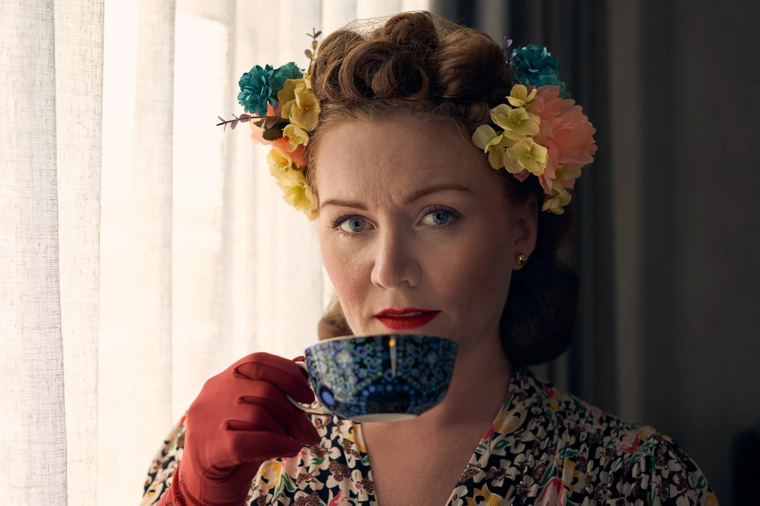 Laura sips from a blue teacup in red gloves