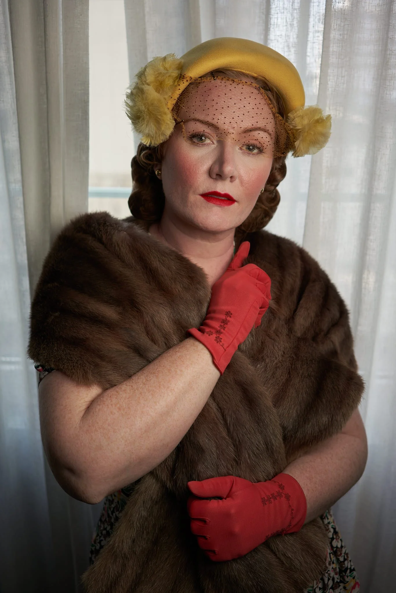 Laura in a yellow hat and fur wrap by a window