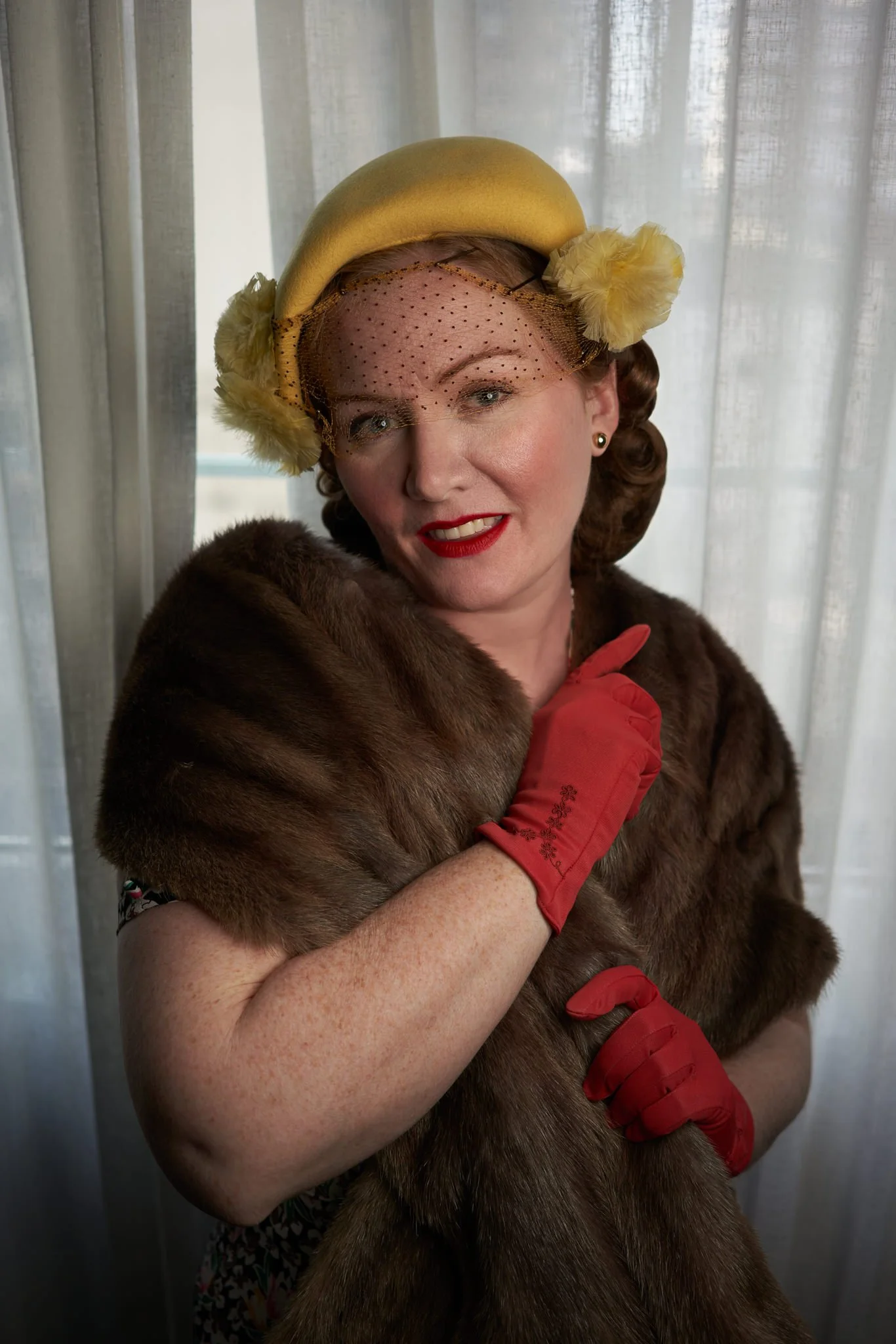 Laura in a yellow hat and fur stole by a curtain