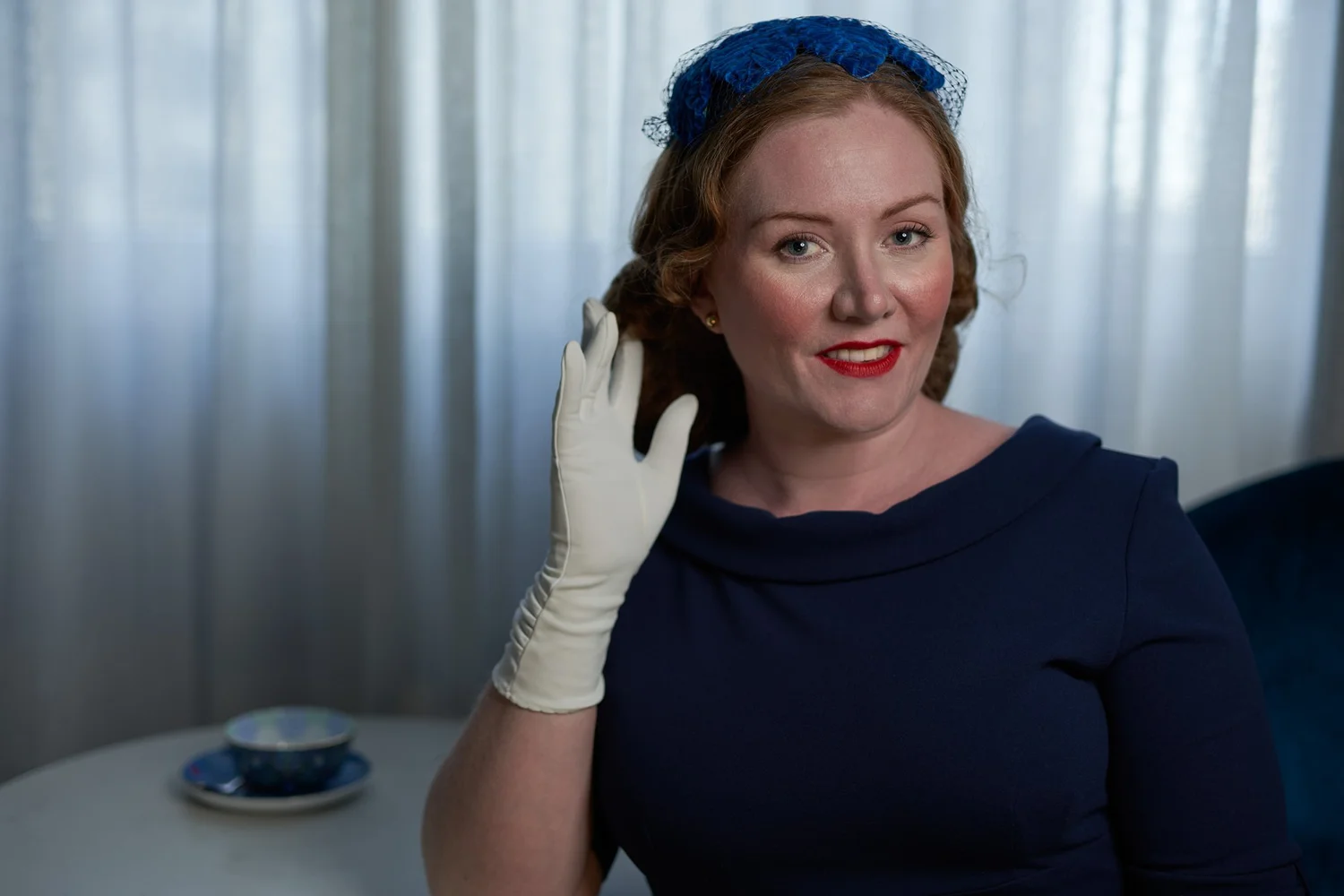 Laura in a navy dress and blue hat with a white glove