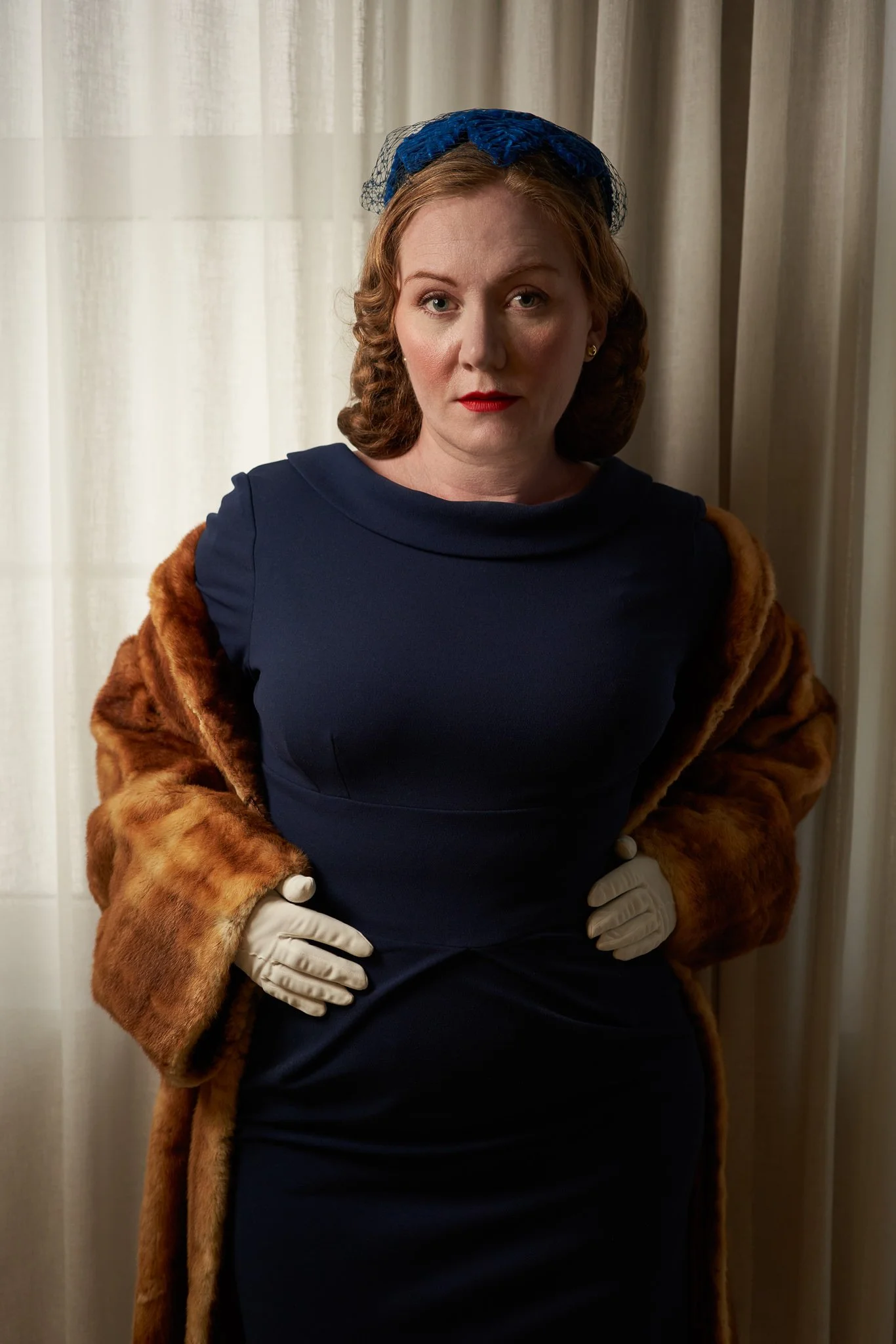 Laura in a navy dress with a fur coat over her shoulders