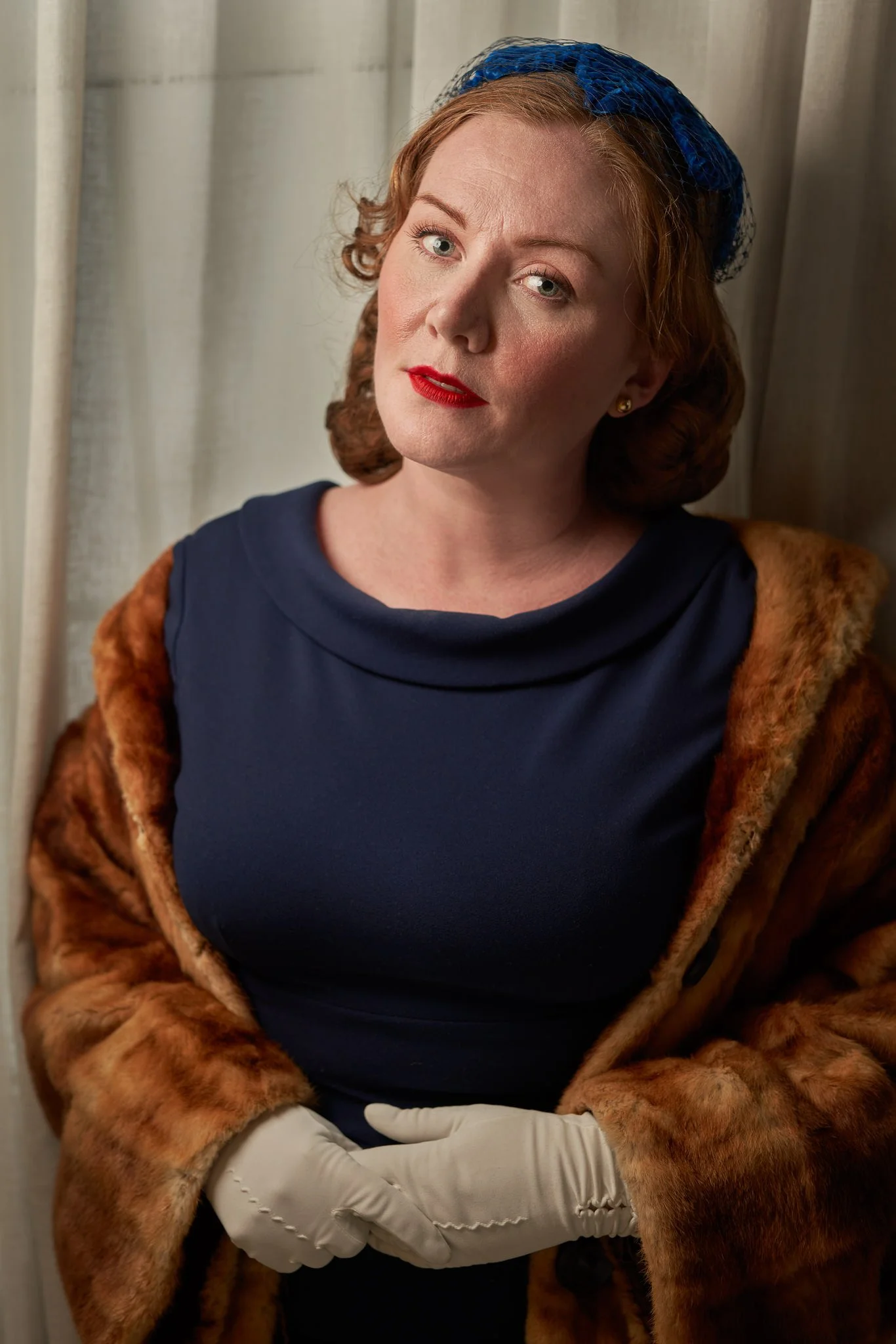 Laura in a navy dress and fur coat with gloved hands clasped