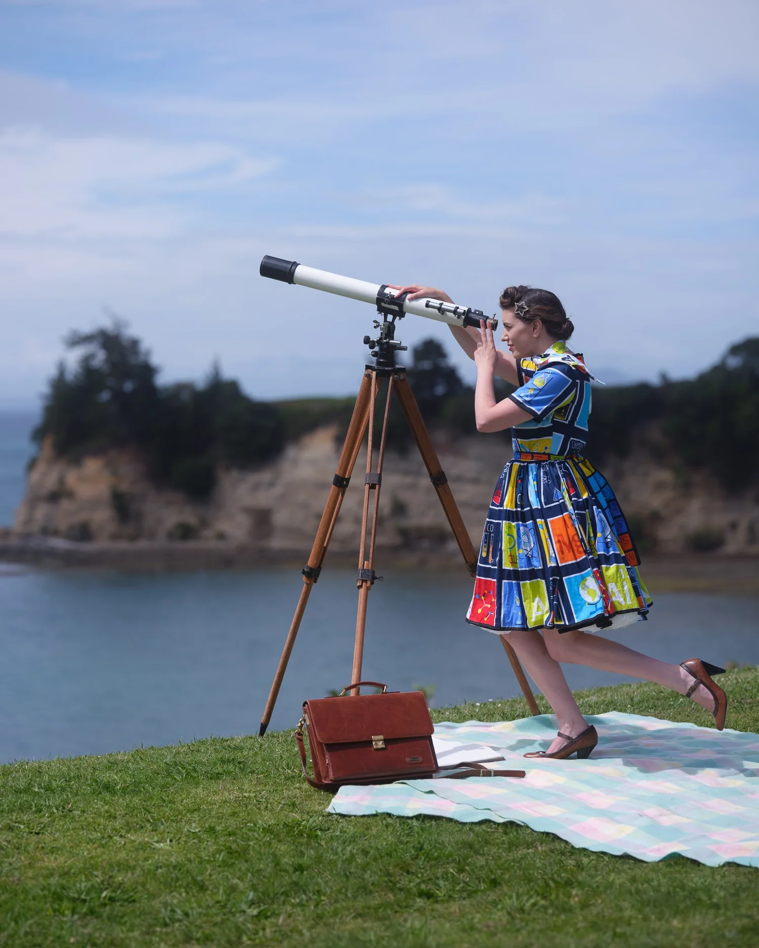 Jay in a colourful dress looks through a telescope on a clifftop
