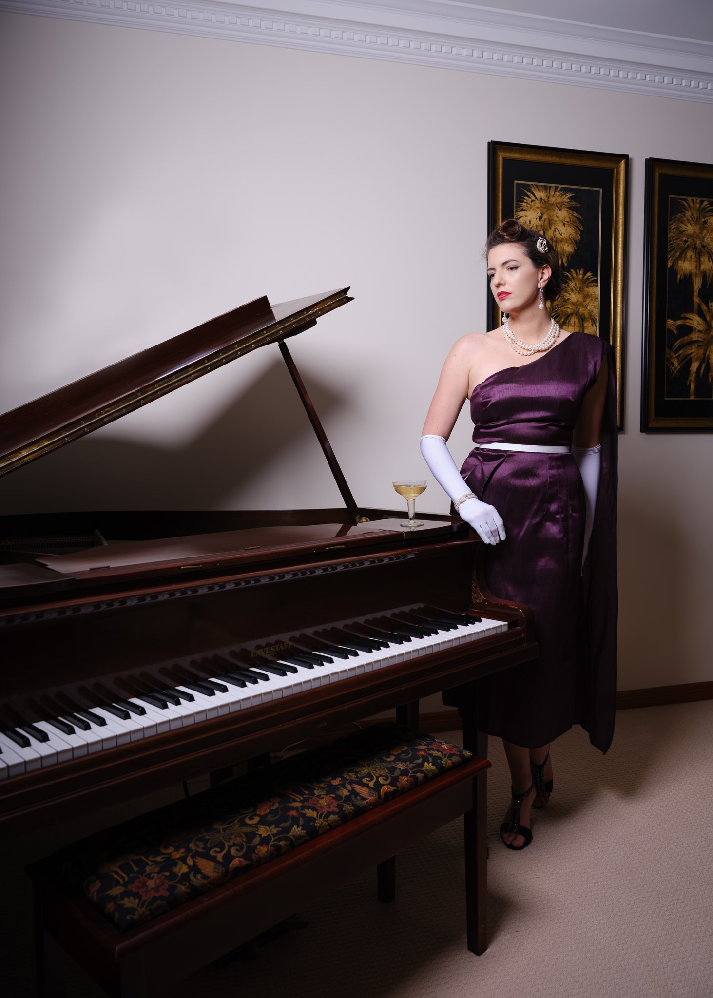 Jay in a purple gown and white gloves beside a grand piano