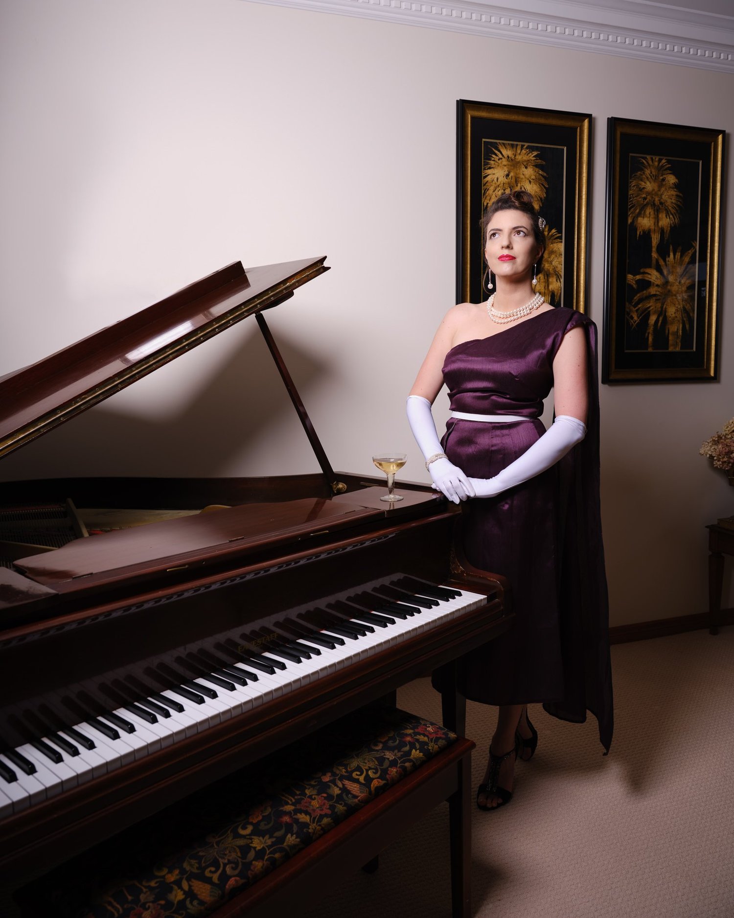 Jay stands at the piano in a purple one-shoulder gown