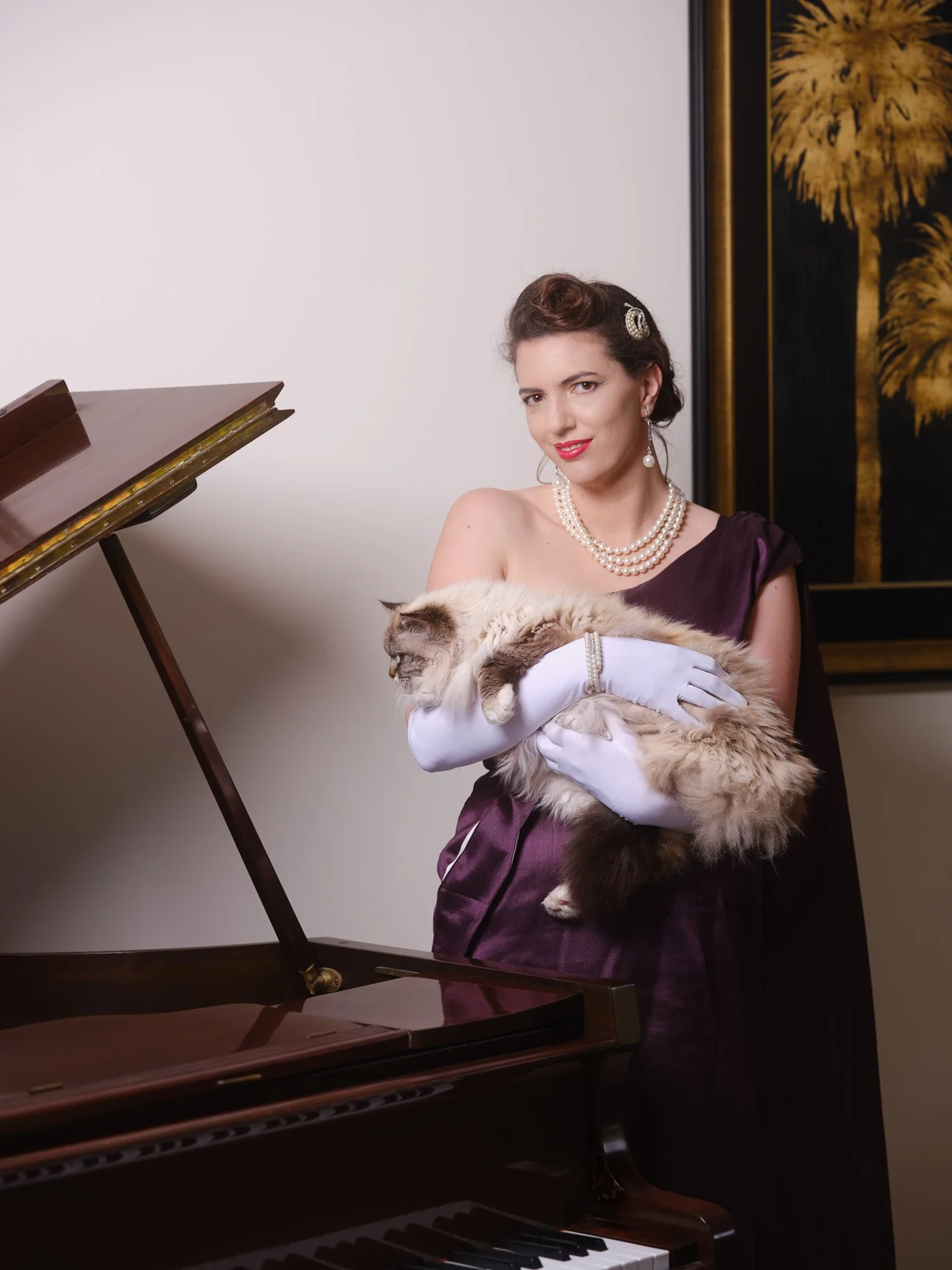 Jay holds a fluffy cat beside the piano