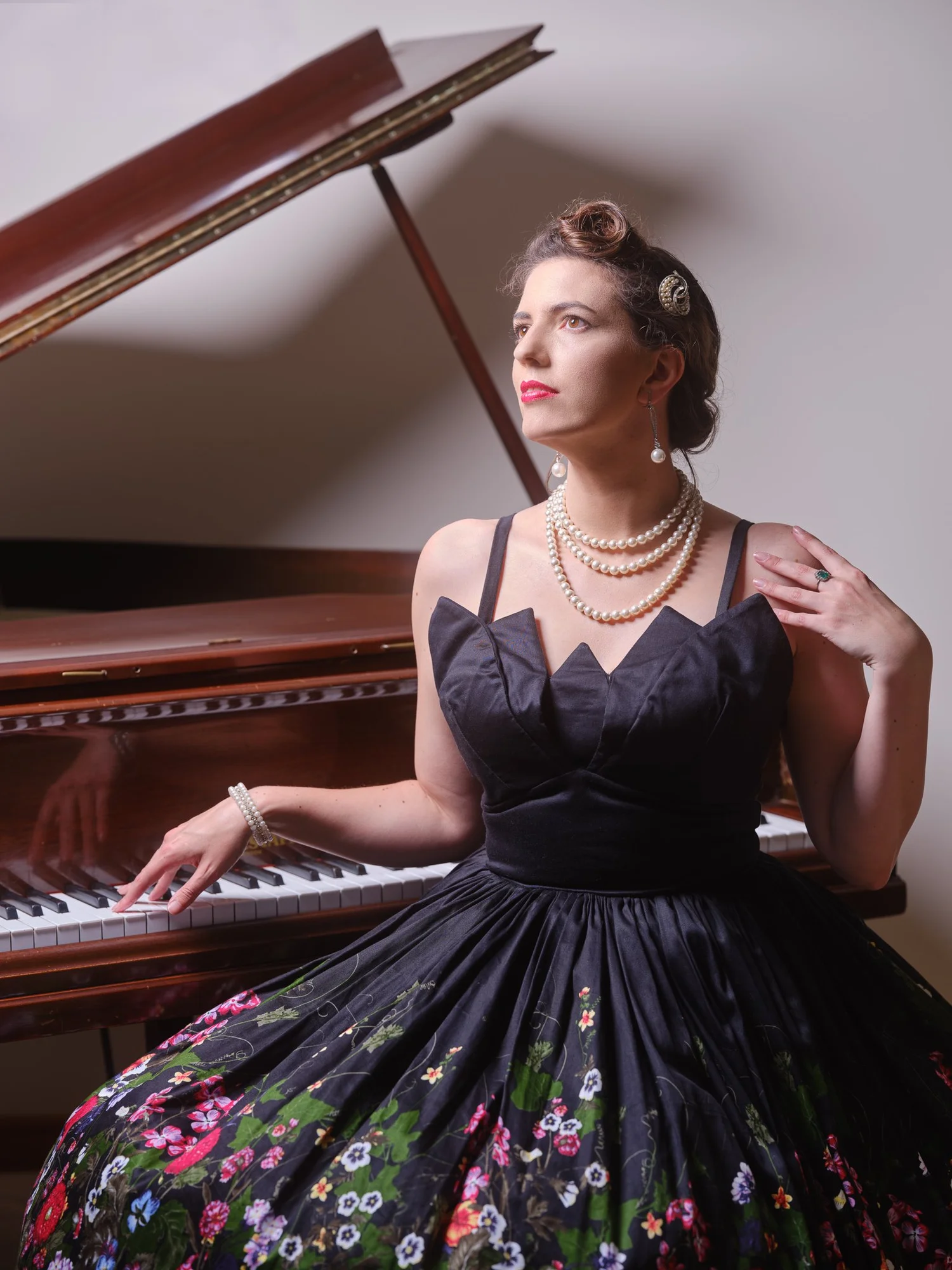 Jay in a floral pin-up dress seated at a grand piano