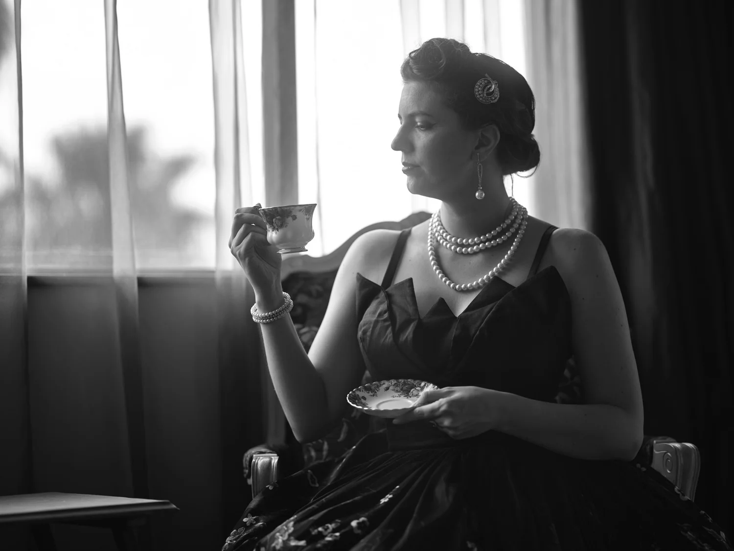 Black and white photo of Jay sipping tea by the window