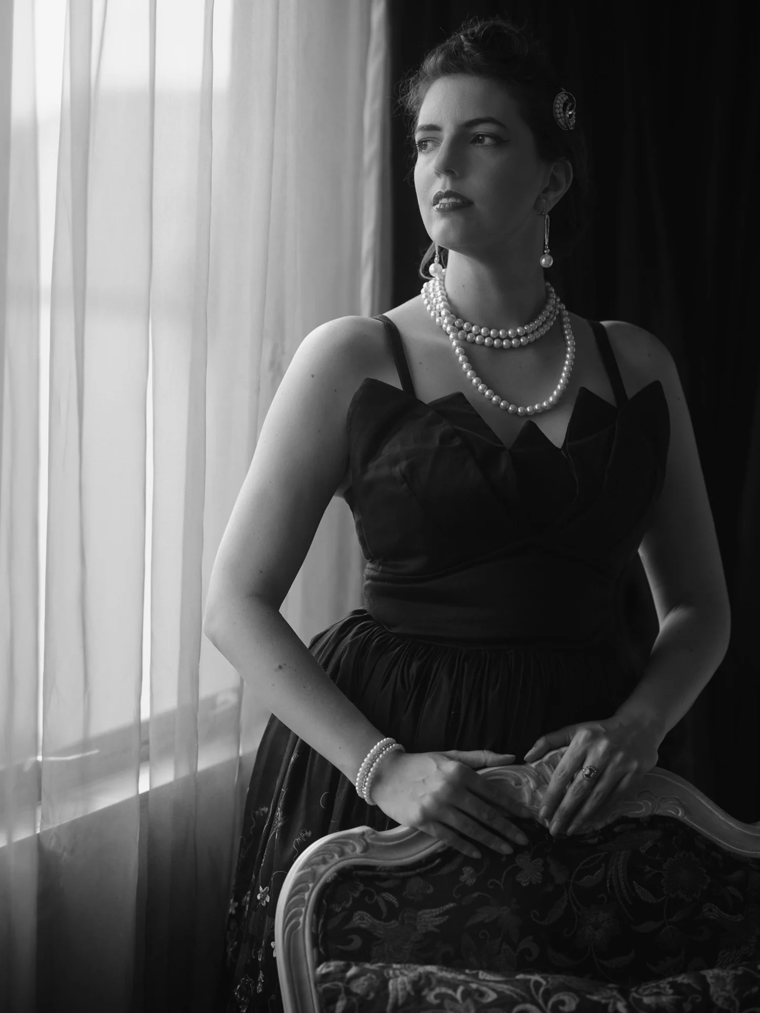 Black and white photo of Jay in pearls seated by a window