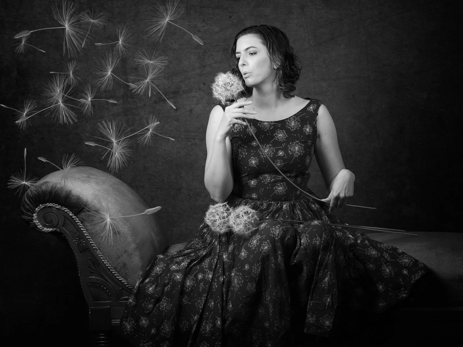 Black and white photo of Jay on a chaise longue blowing a dandelion
