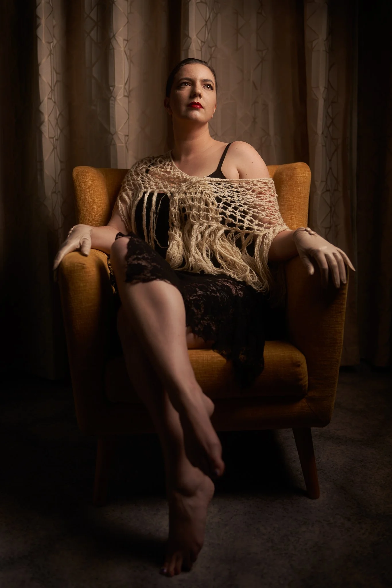 Jay in a fringed flapper dress on a mustard armchair