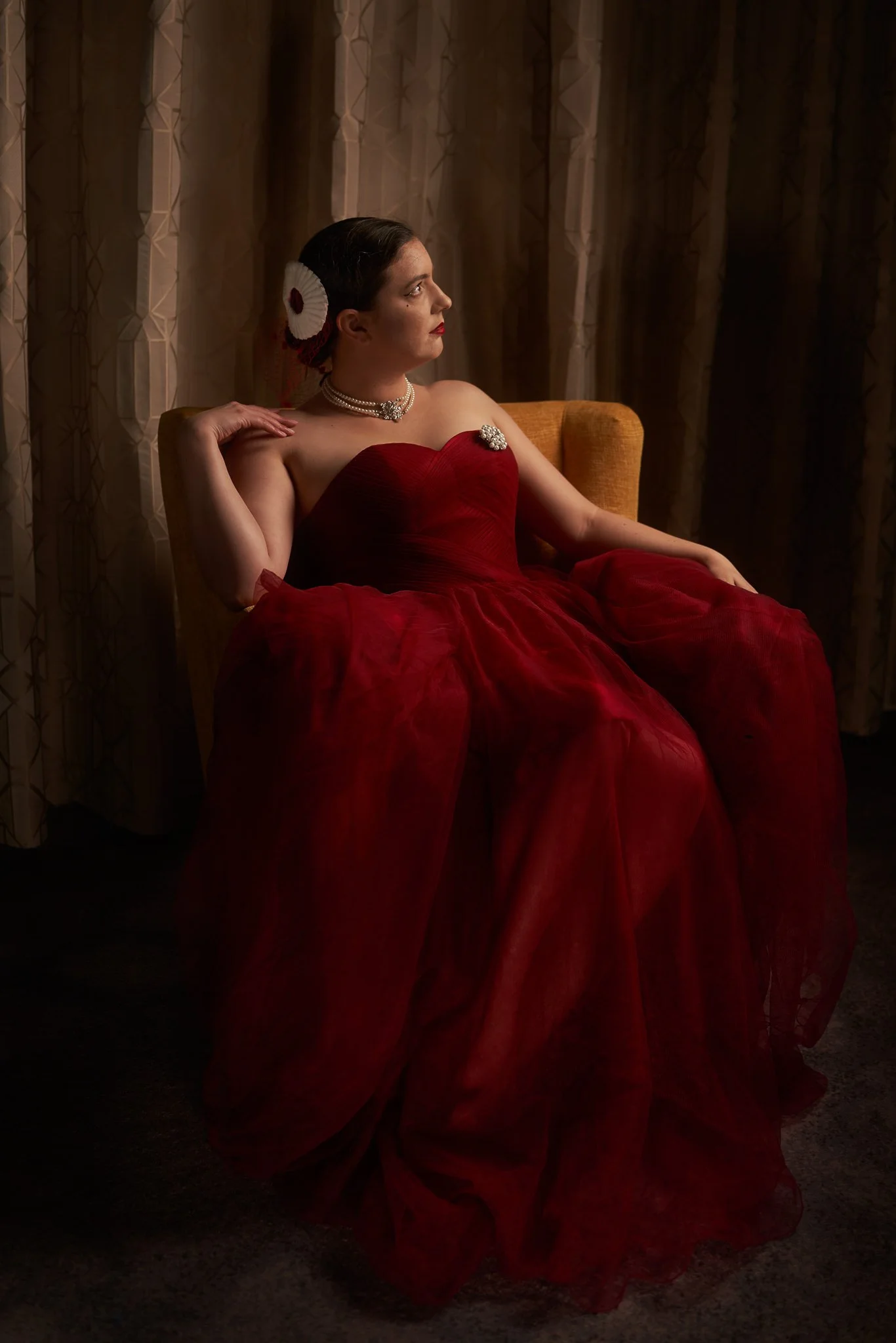Jay in a red tulle gown on a mustard armchair
