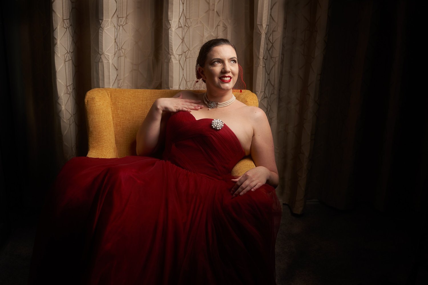 Jay in a strapless red gown seated in low light