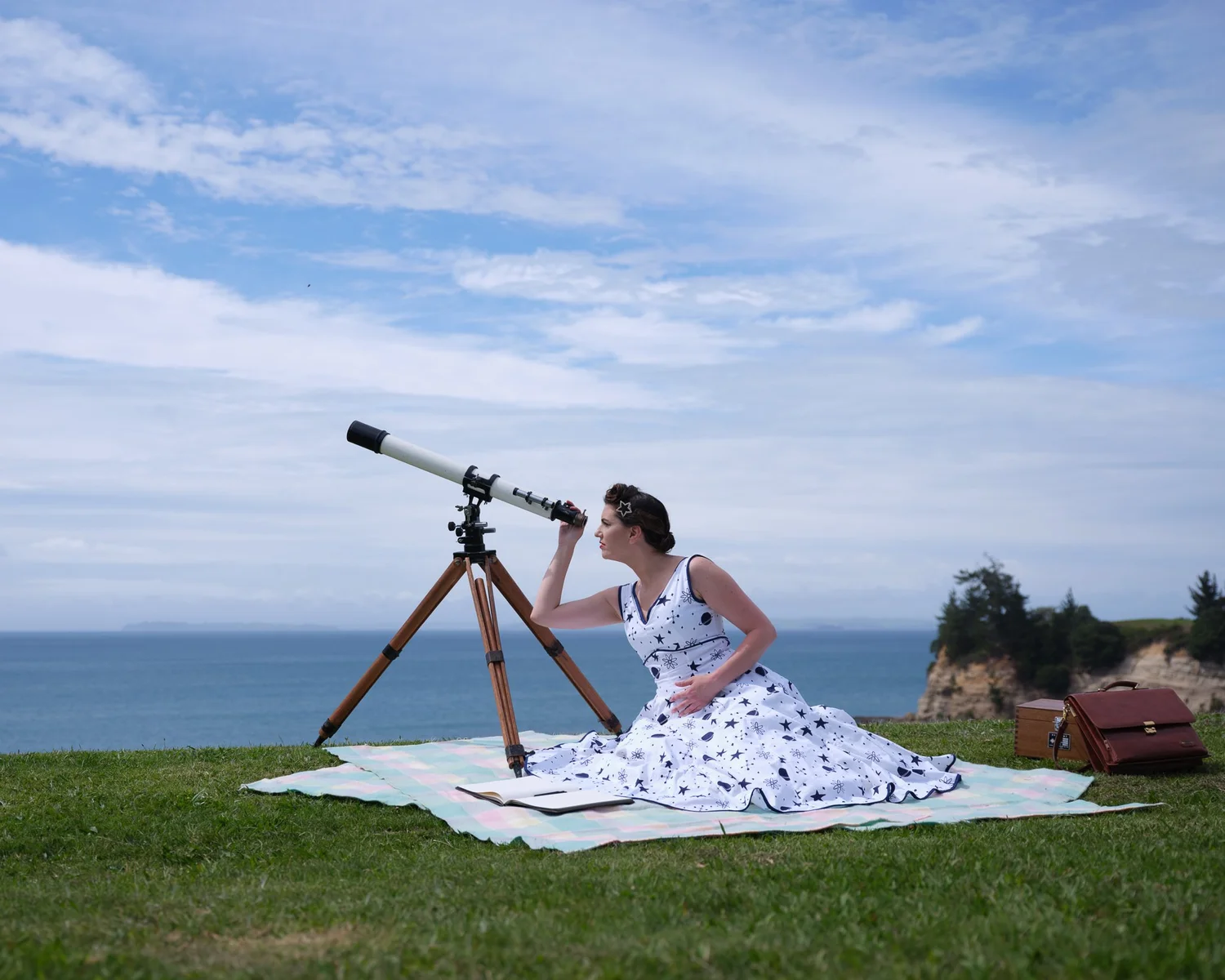 Jay looks through a telescope while sitting on a picnic blanket