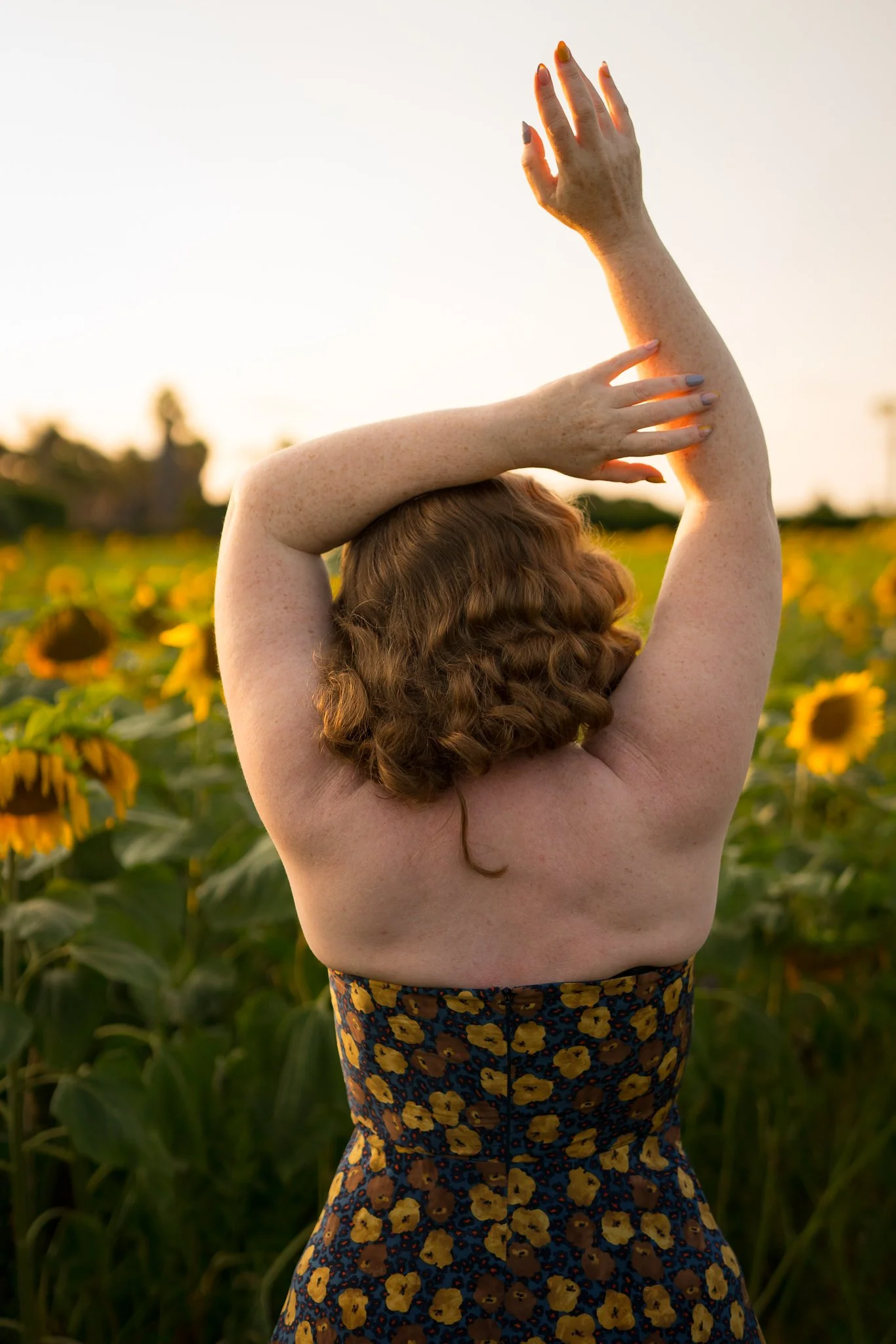 A model with arms raised among the sunflowers seen from behind