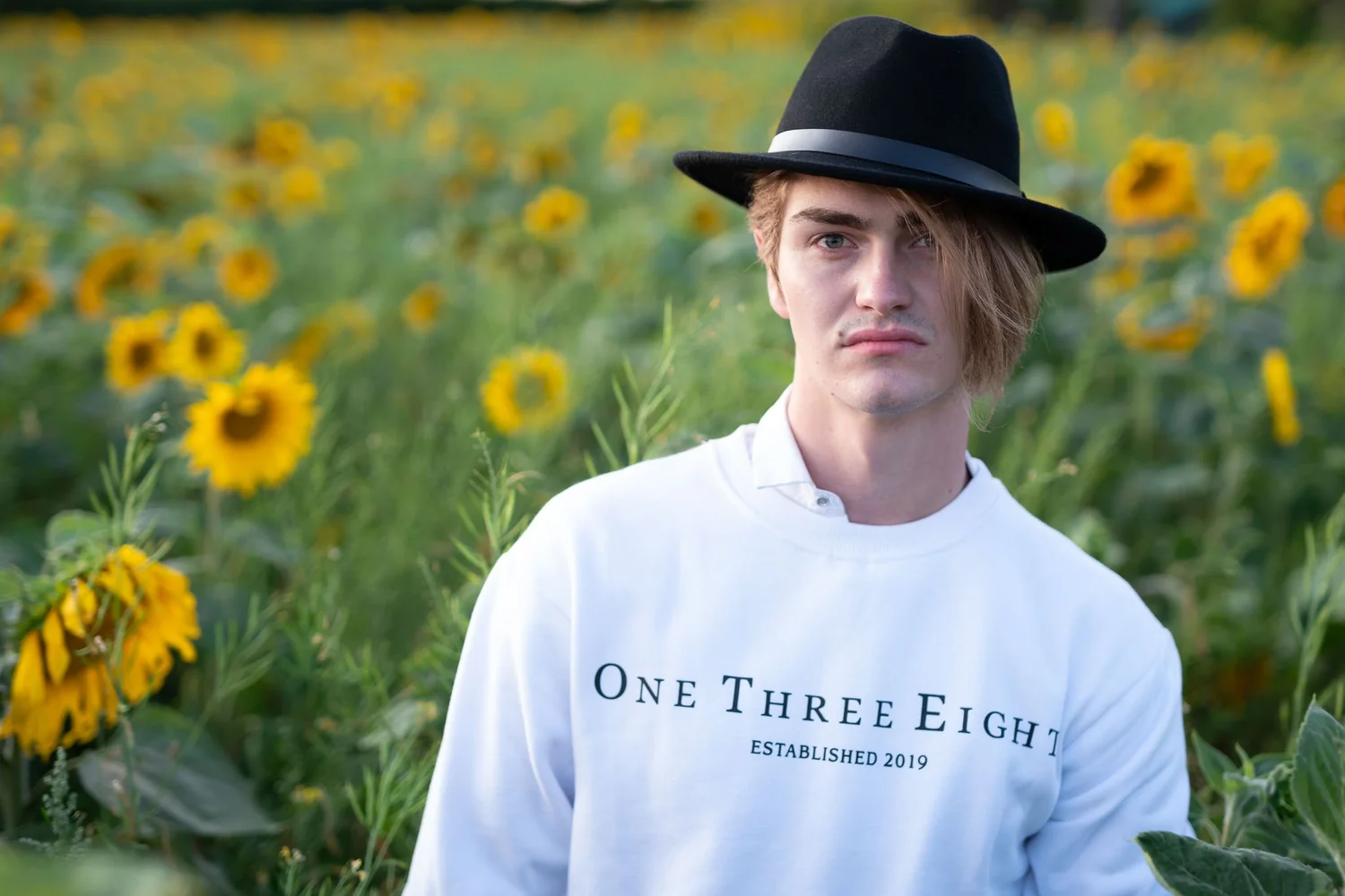 A young man in a black hat in the sunflower field at dusk