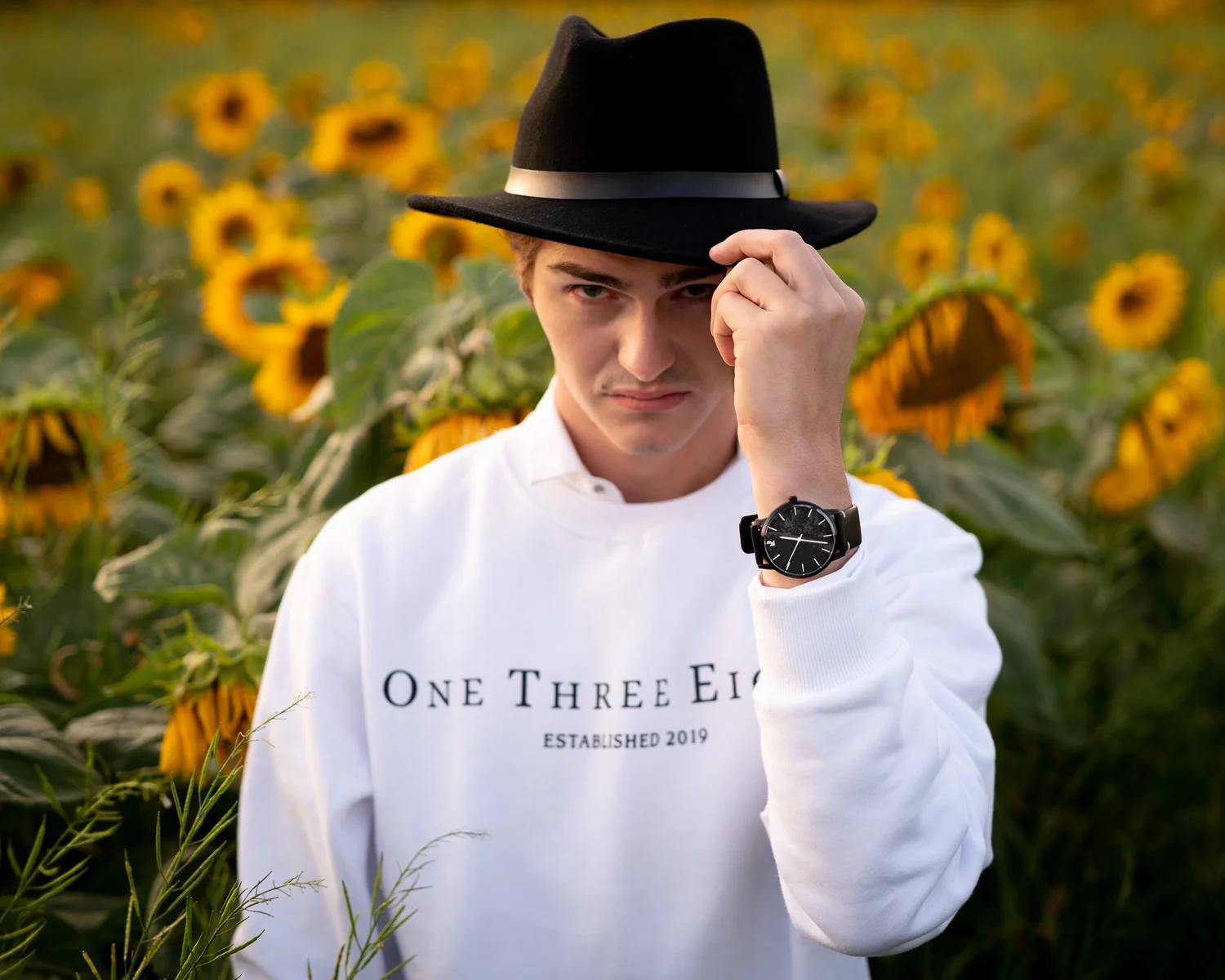 A young man in a black hat and white jumper in the sunflower field