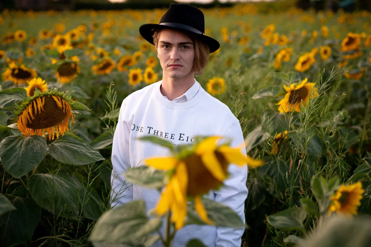A young man in a black hat behind a sunflower