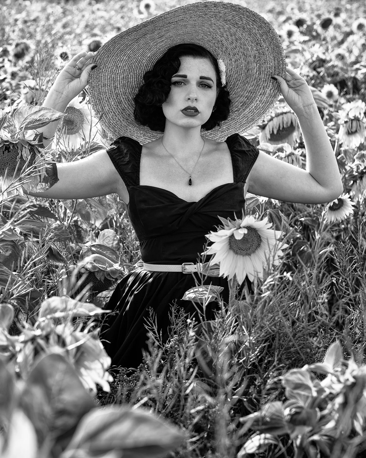 Black and white photo of a model in a straw hat among sunflowers