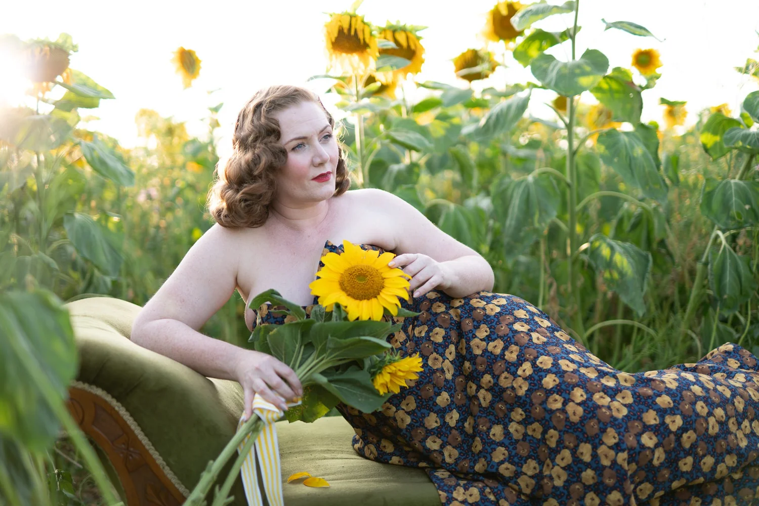 A model reclines on a green sofa in the sunflower field