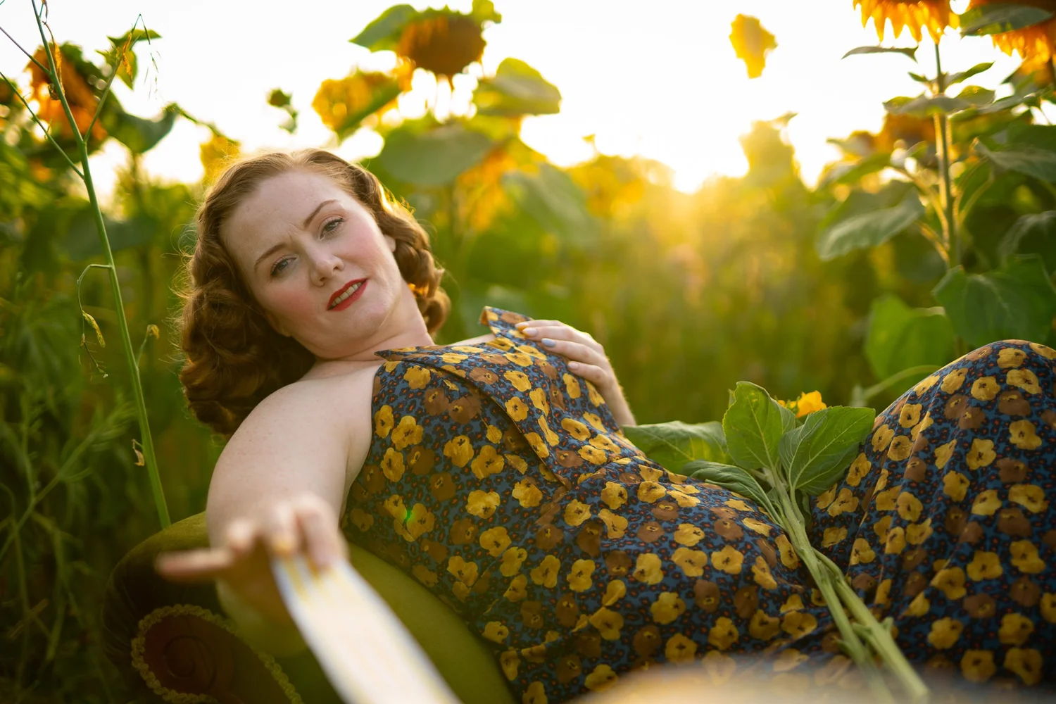 A model reclines on a sofa among sunflowers at golden hour