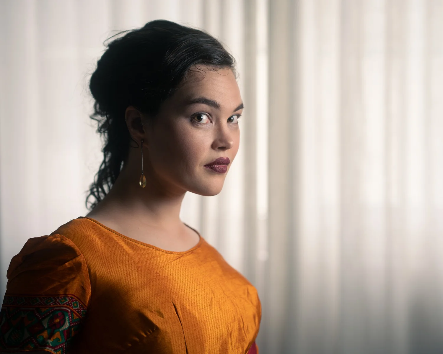 Anita in an orange dress by a sheer curtain