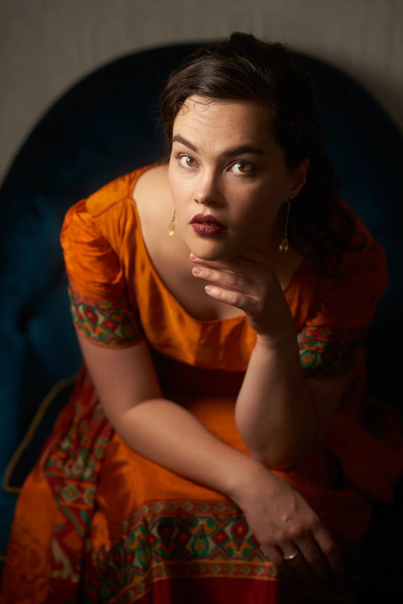 Anita in an orange embroidered dress resting her chin on her hand