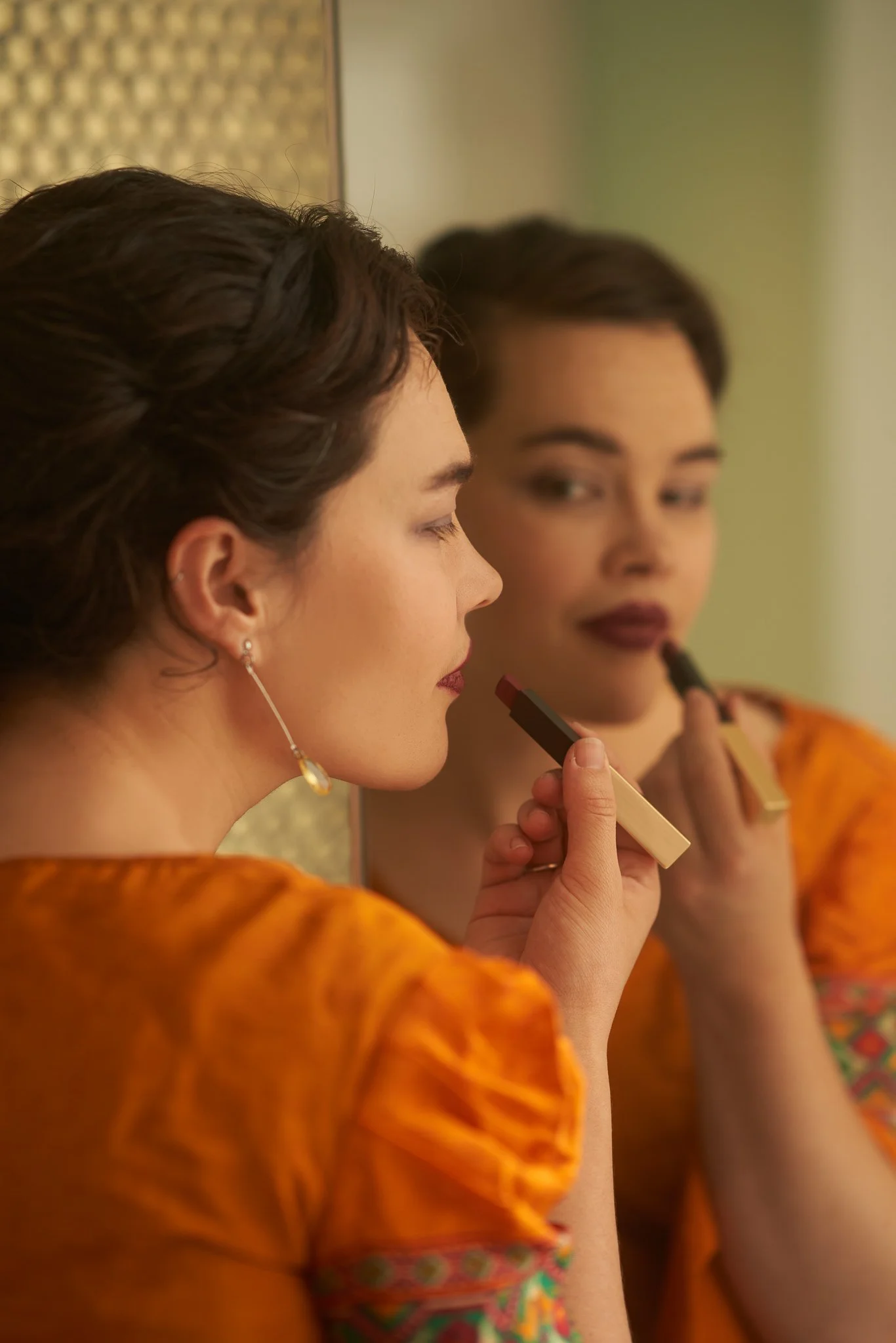 Anita applies lipstick in a mirror while wearing an orange dress