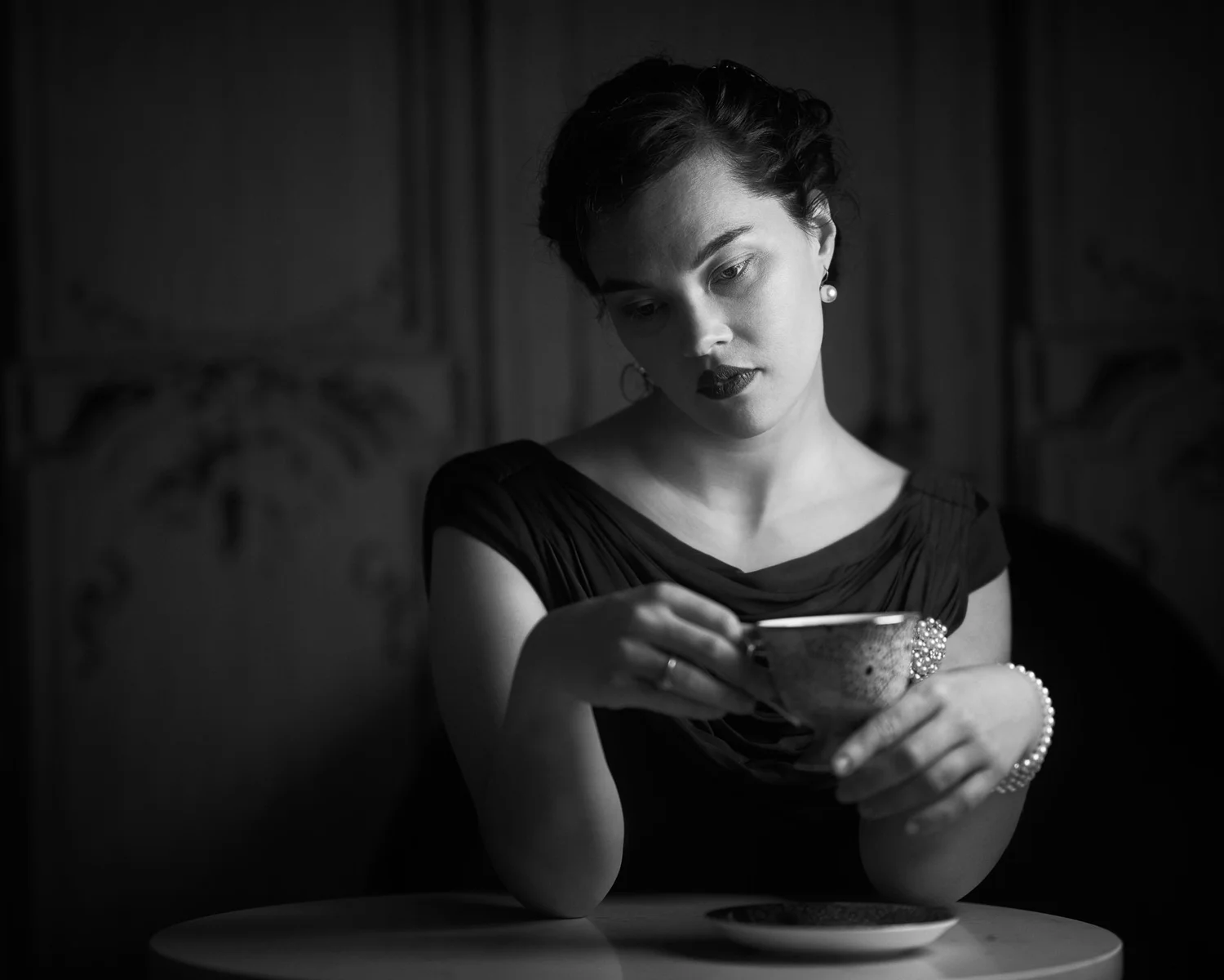 Black and white photo of Anita holding a teacup at a small table