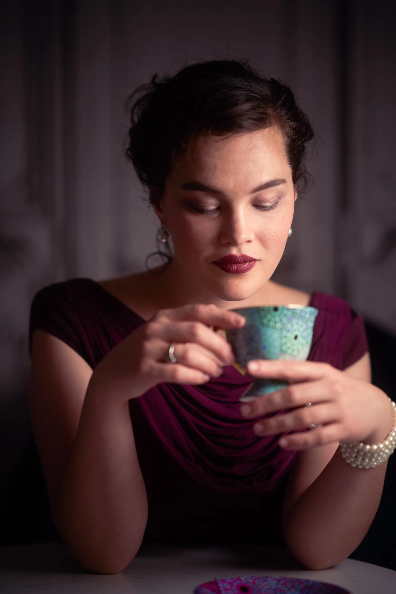 Anita in burgundy holding a teacup and looking down